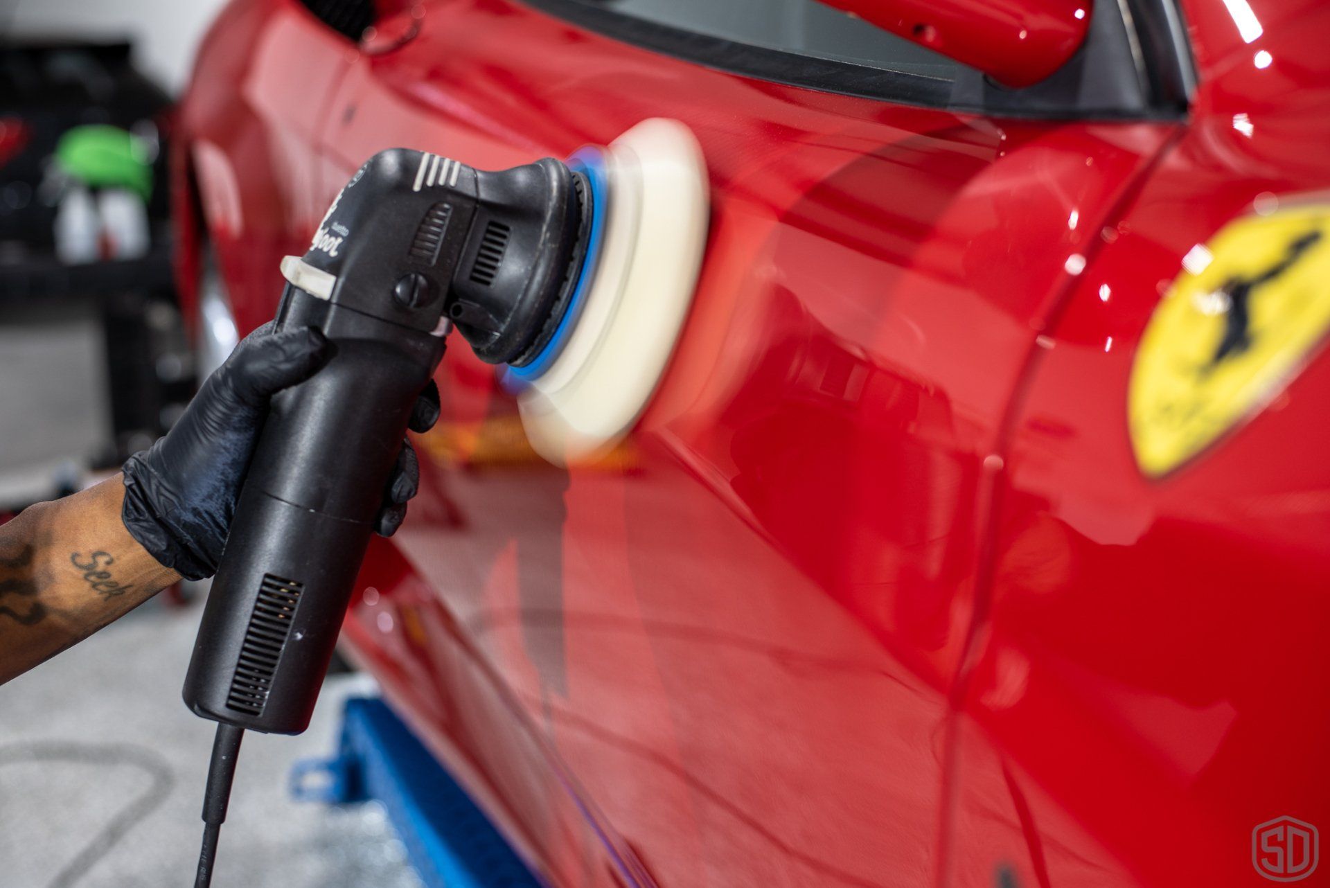 A person is polishing a red ferrari with a machine.