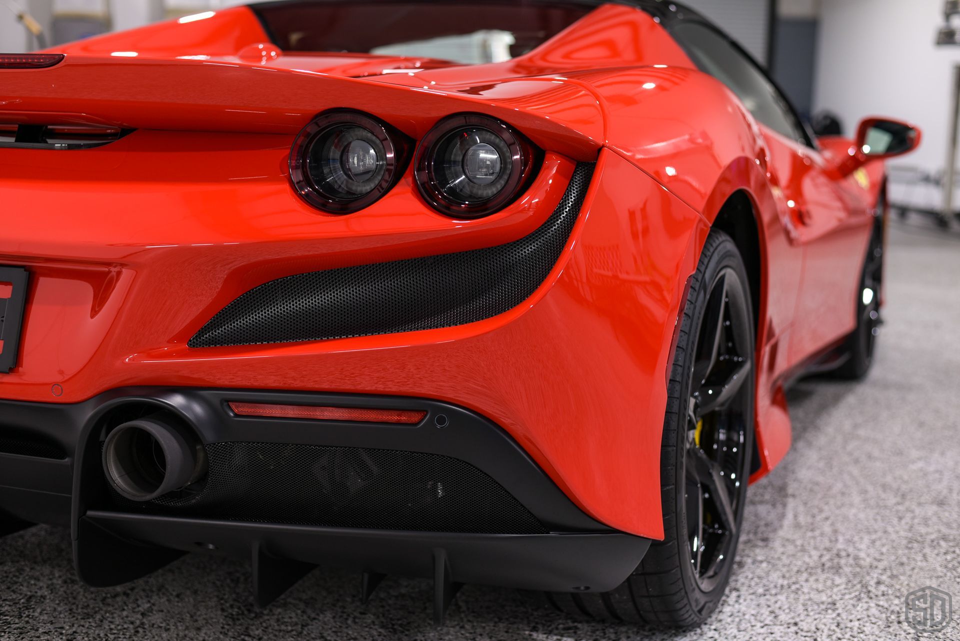 The rear end of a red sports car is shown in a garage.