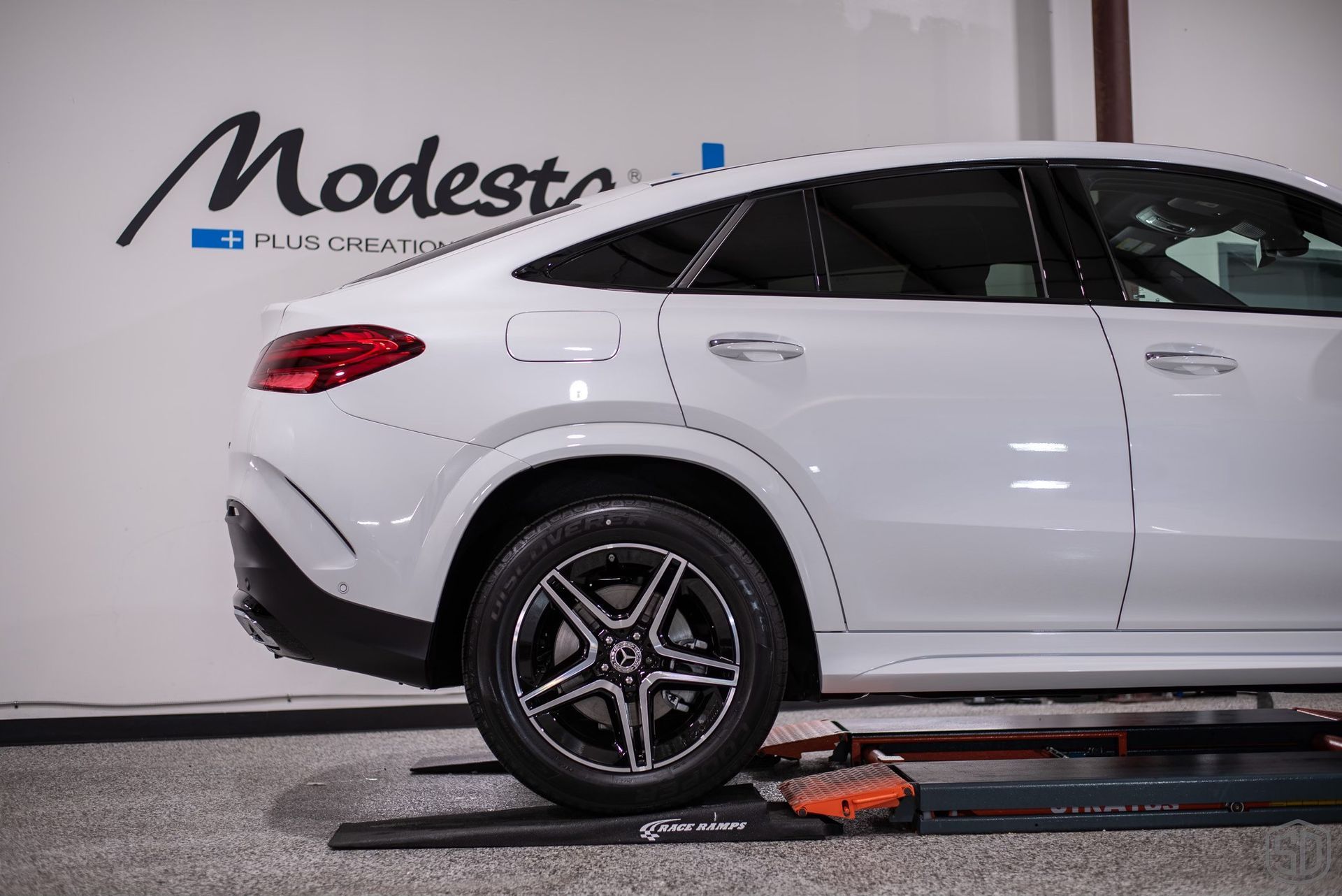 A white car is sitting on a lift in a garage.