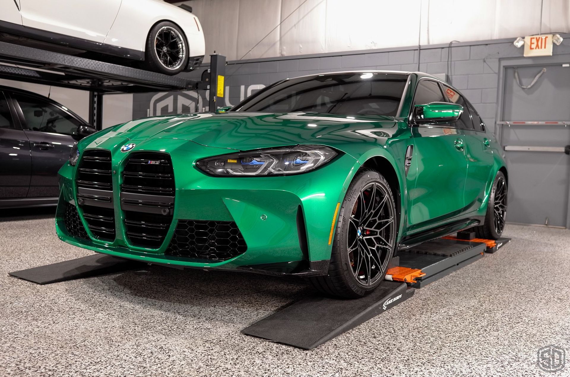 A green bmw m3 is parked on a ramp in a garage.