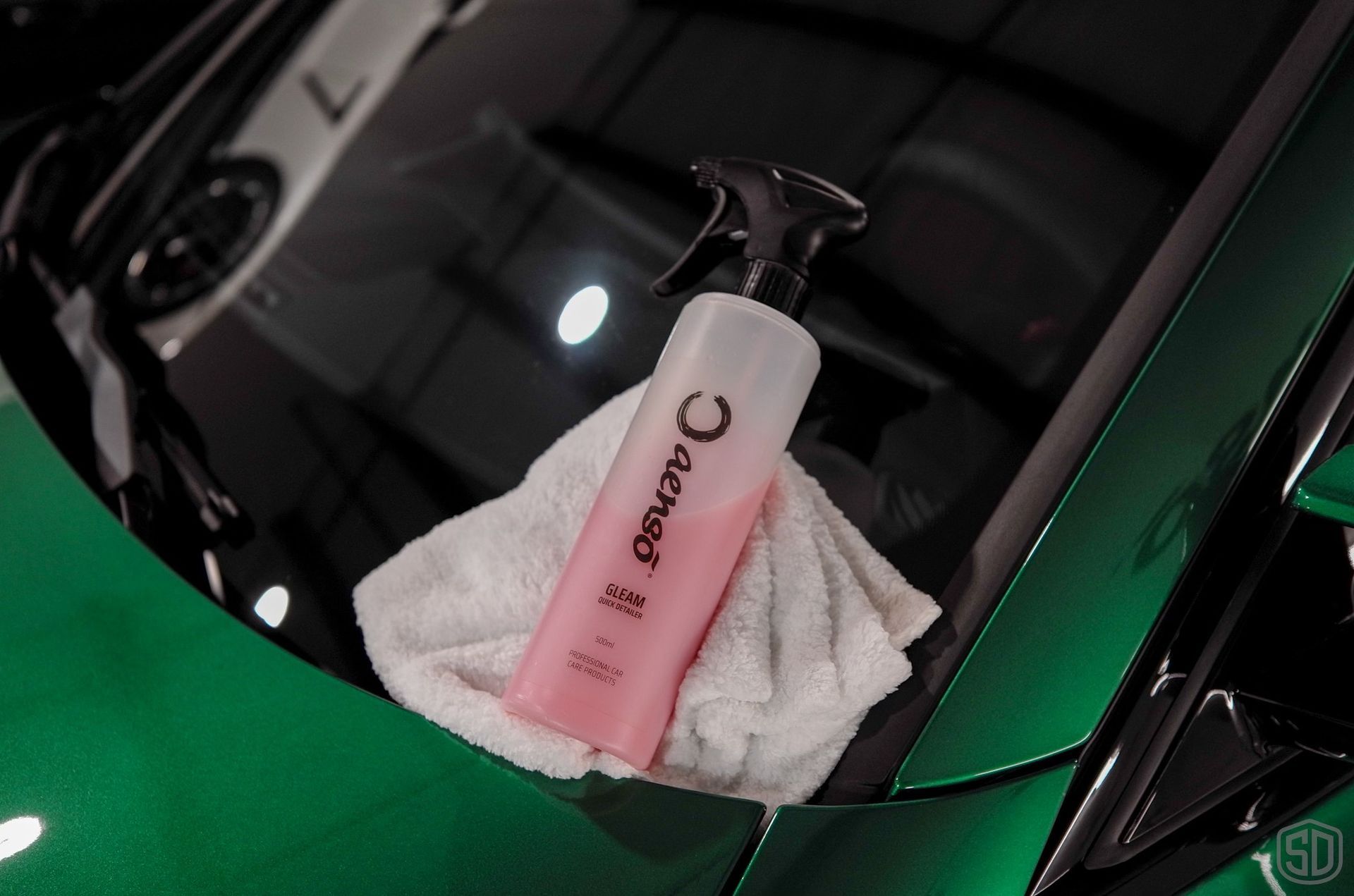 A bottle of cleaner is sitting on a towel on the hood of a green car.