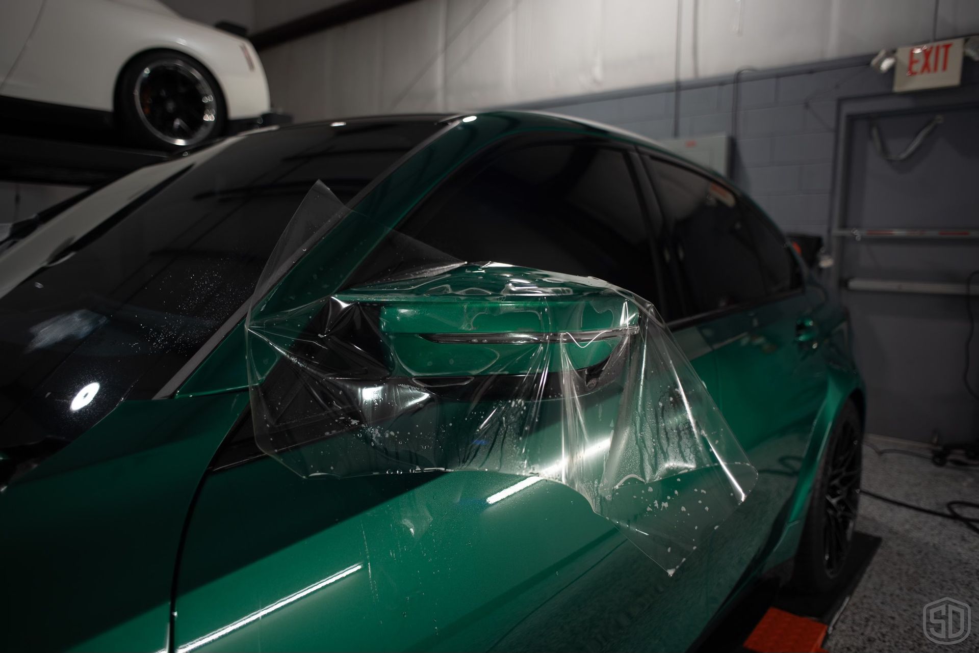 A green car is wrapped in plastic in a garage.