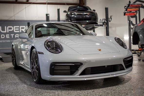 Front end of a white porsche 911 is parked in a garage.