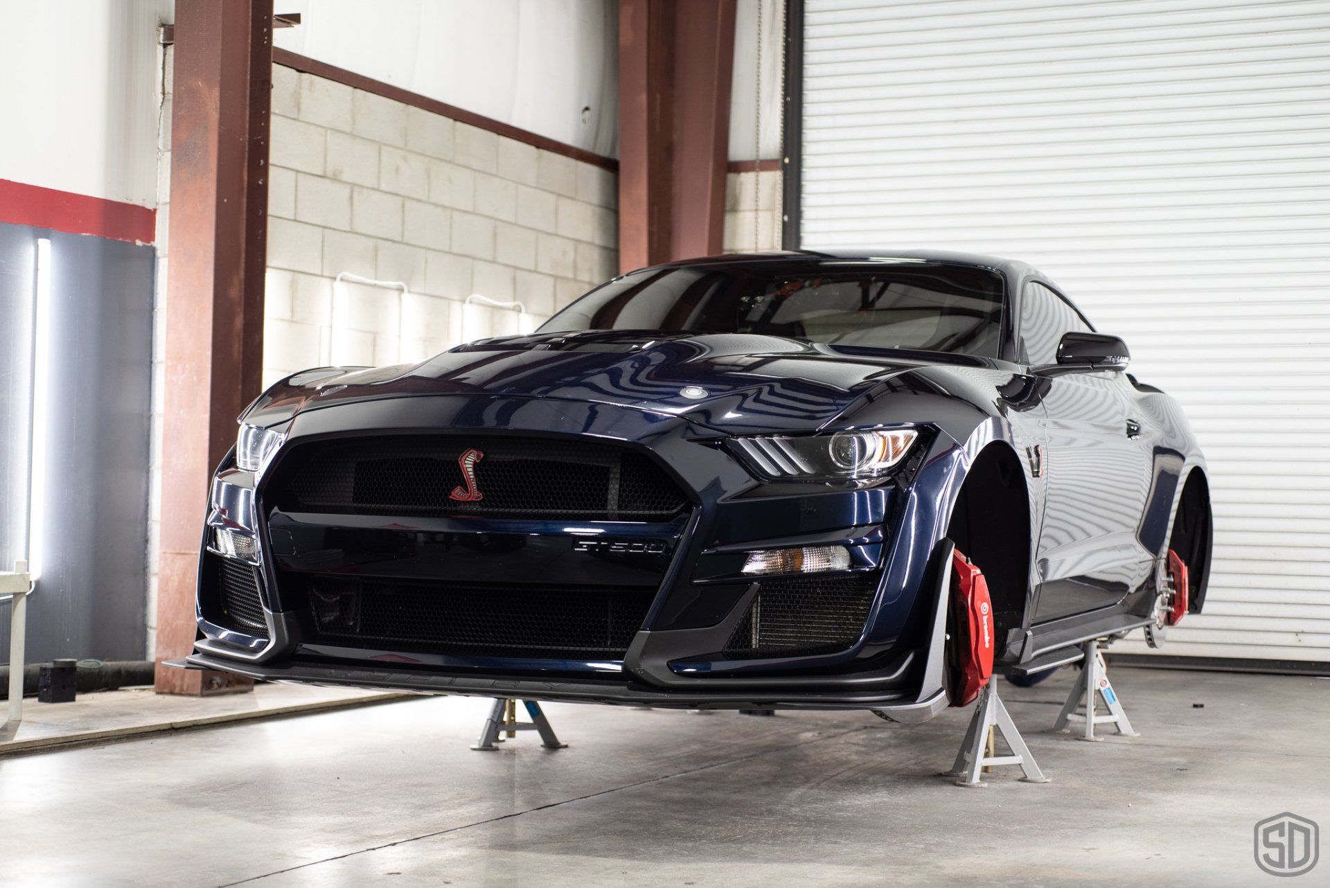 A black ford mustang is sitting on a set of jack stands in a garage.