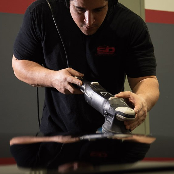 A man wearing a black sd shirt is polishing a car