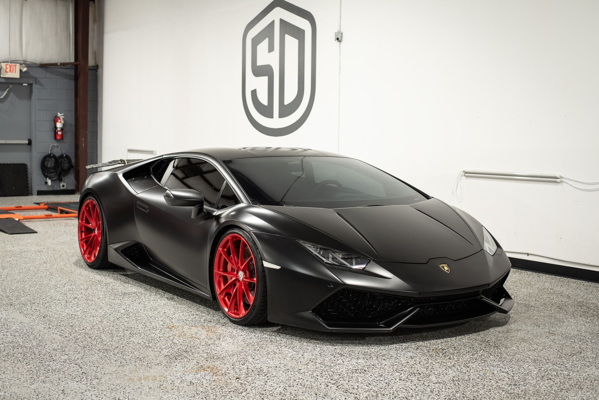 A black lamborghini huracan with red wheels is parked in a garage.