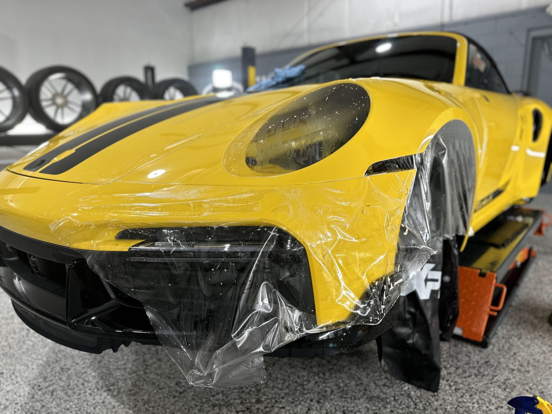 A yellow sports car is wrapped in plastic and sitting on a tow truck.