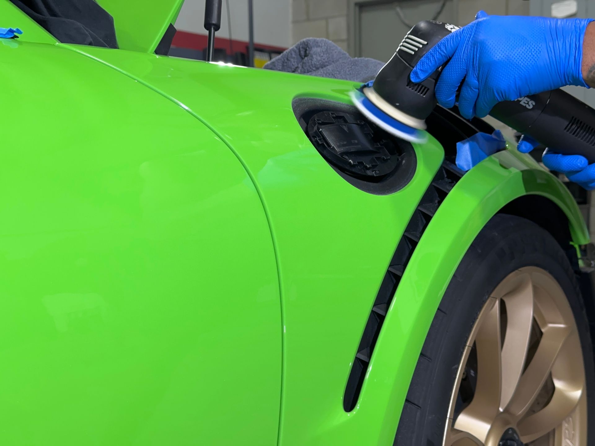 A person is polishing a green car with a machine.
