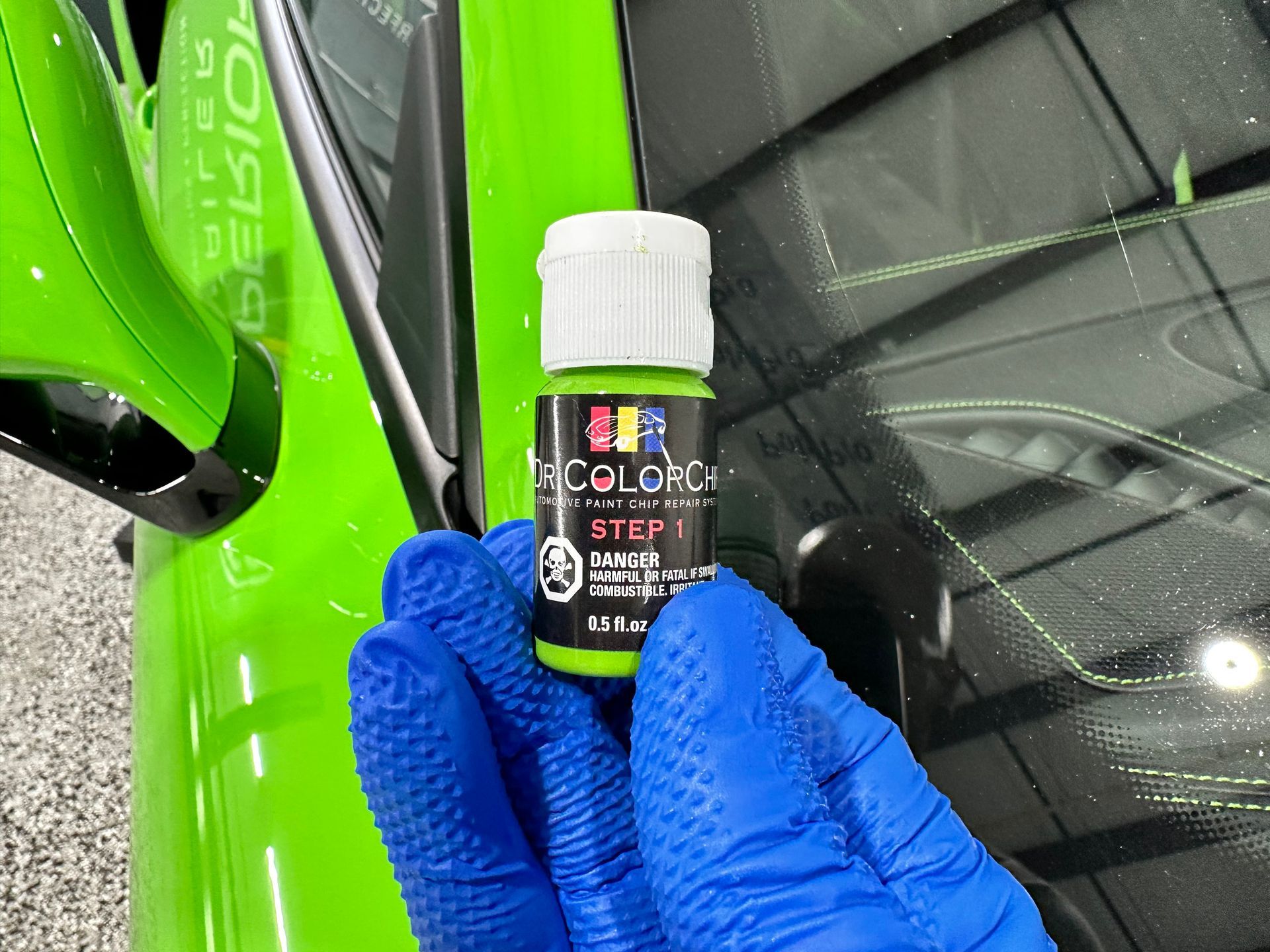 A person is holding a bottle of green paint in front of a green car.