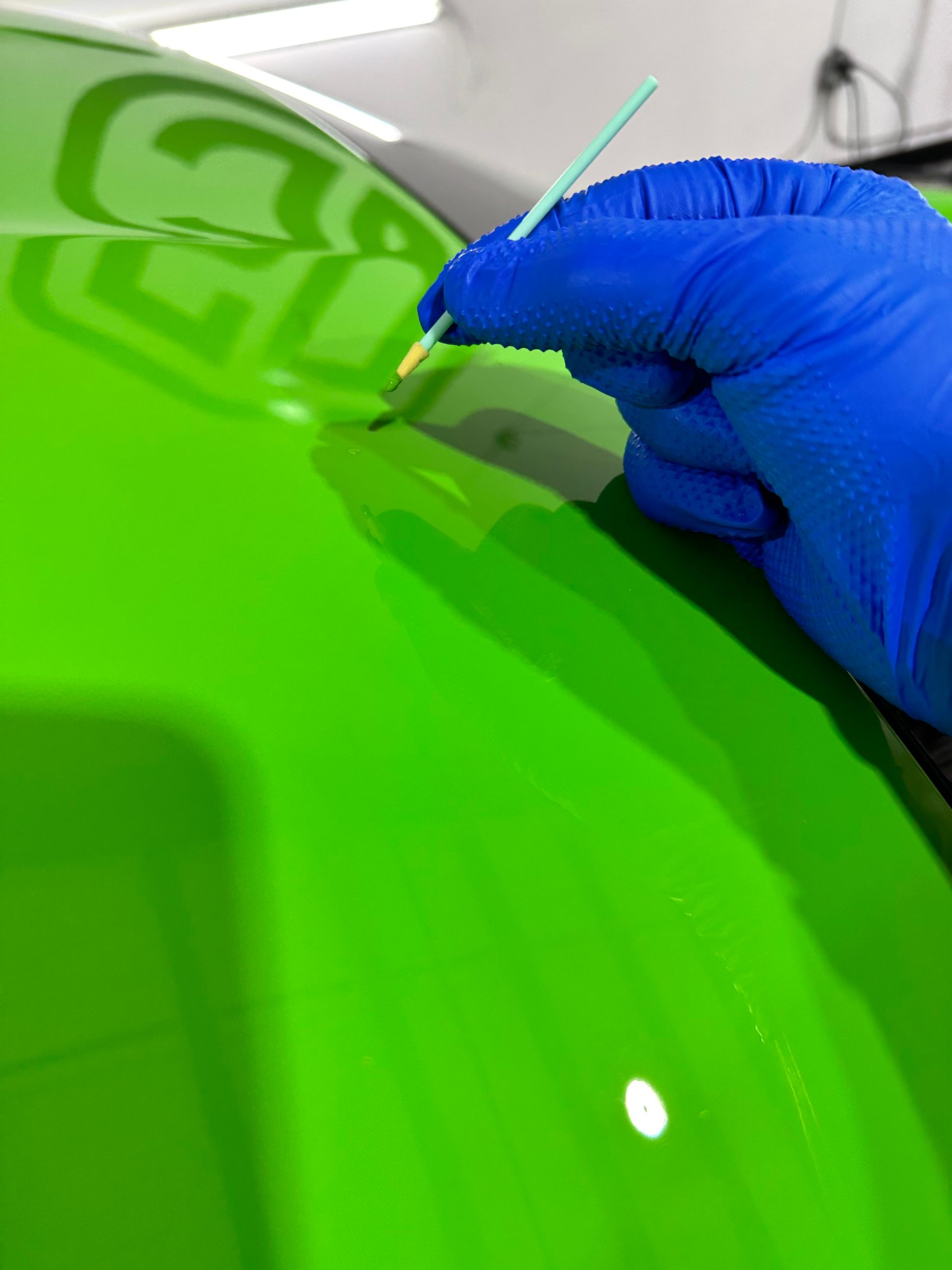 A person wearing blue gloves is painting a green car with a brush.