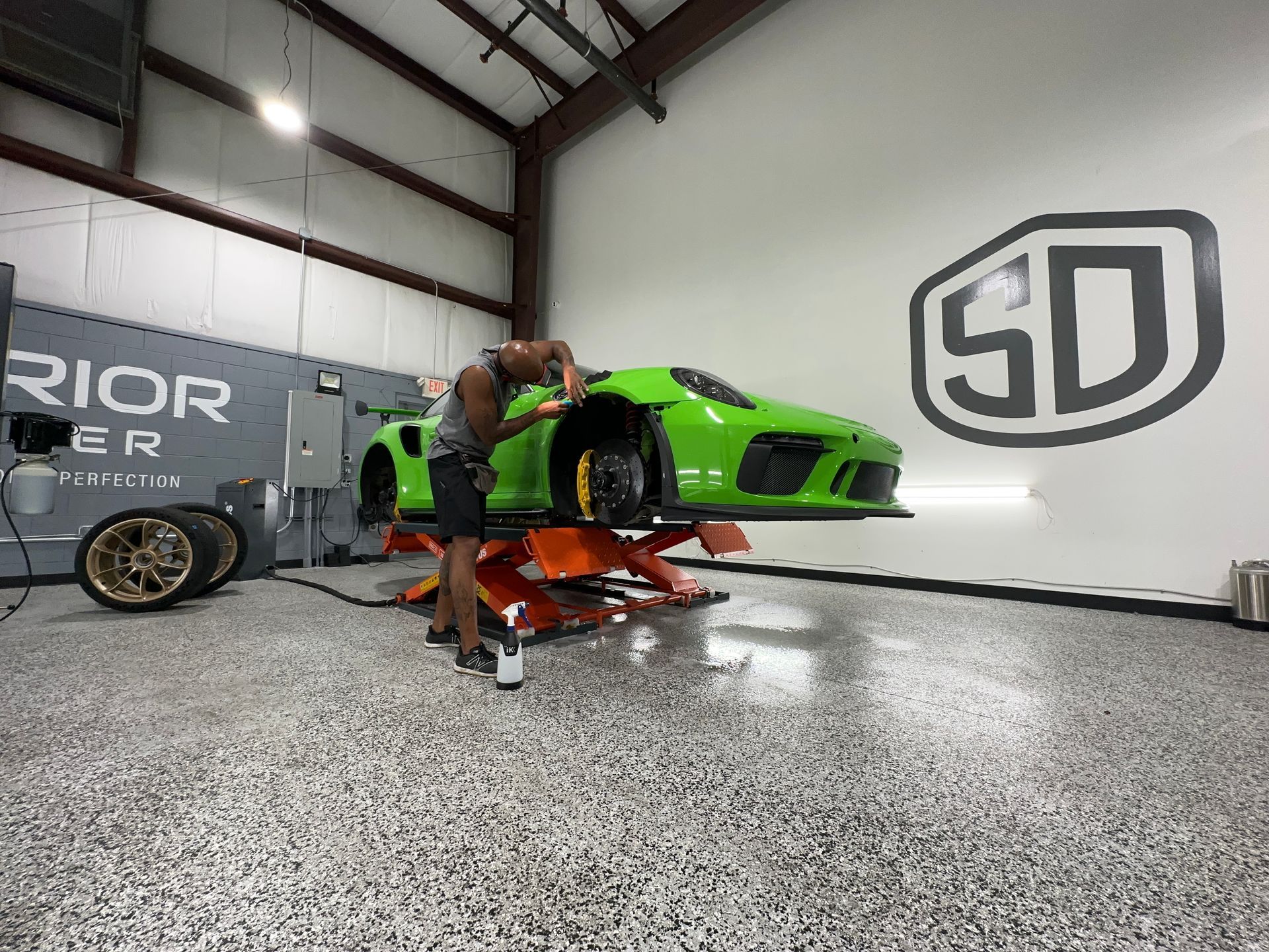 A man is working on a green sports car on a lift in a garage.