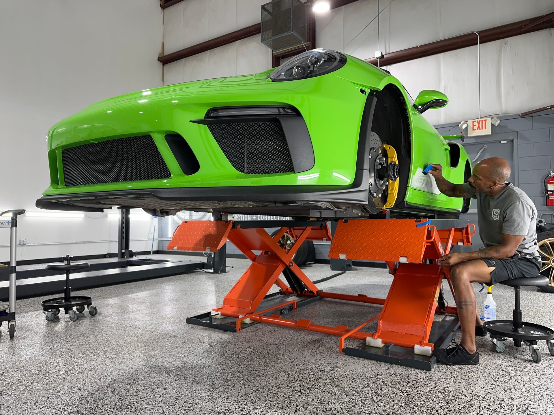 A man is working on a green sports car on a lift in a garage.