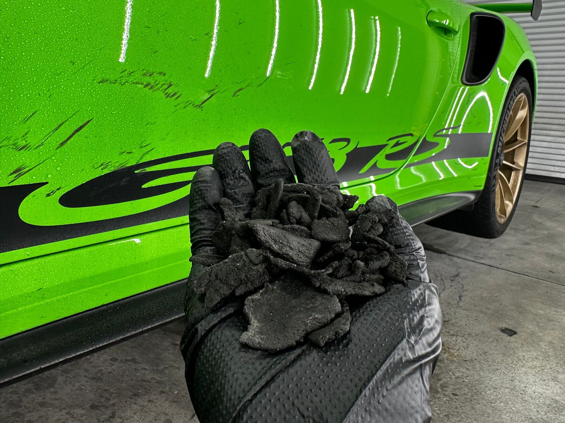 A person is holding a pile of dirt in front of a green car.