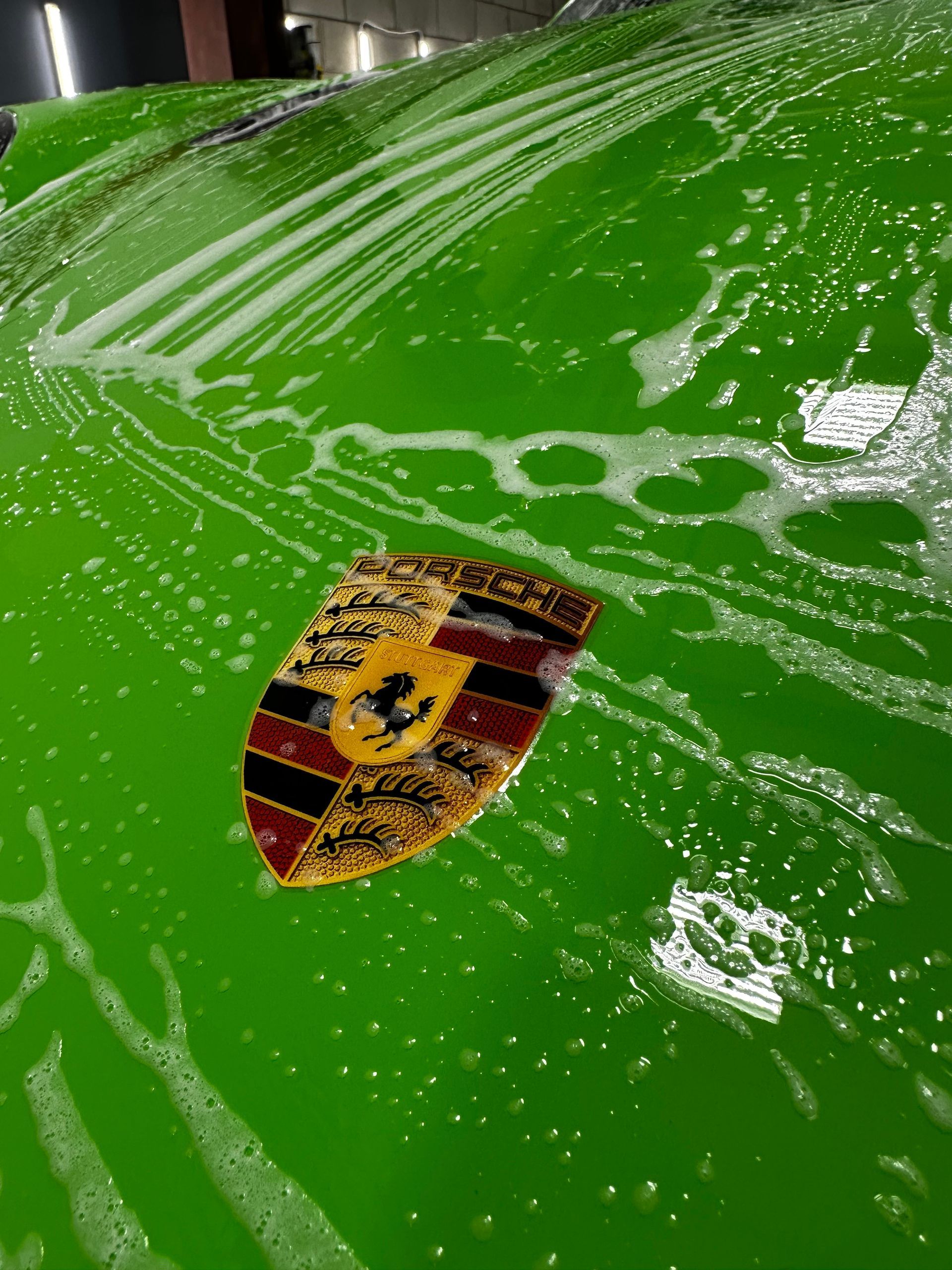 A green porsche car is being washed with soap and water.