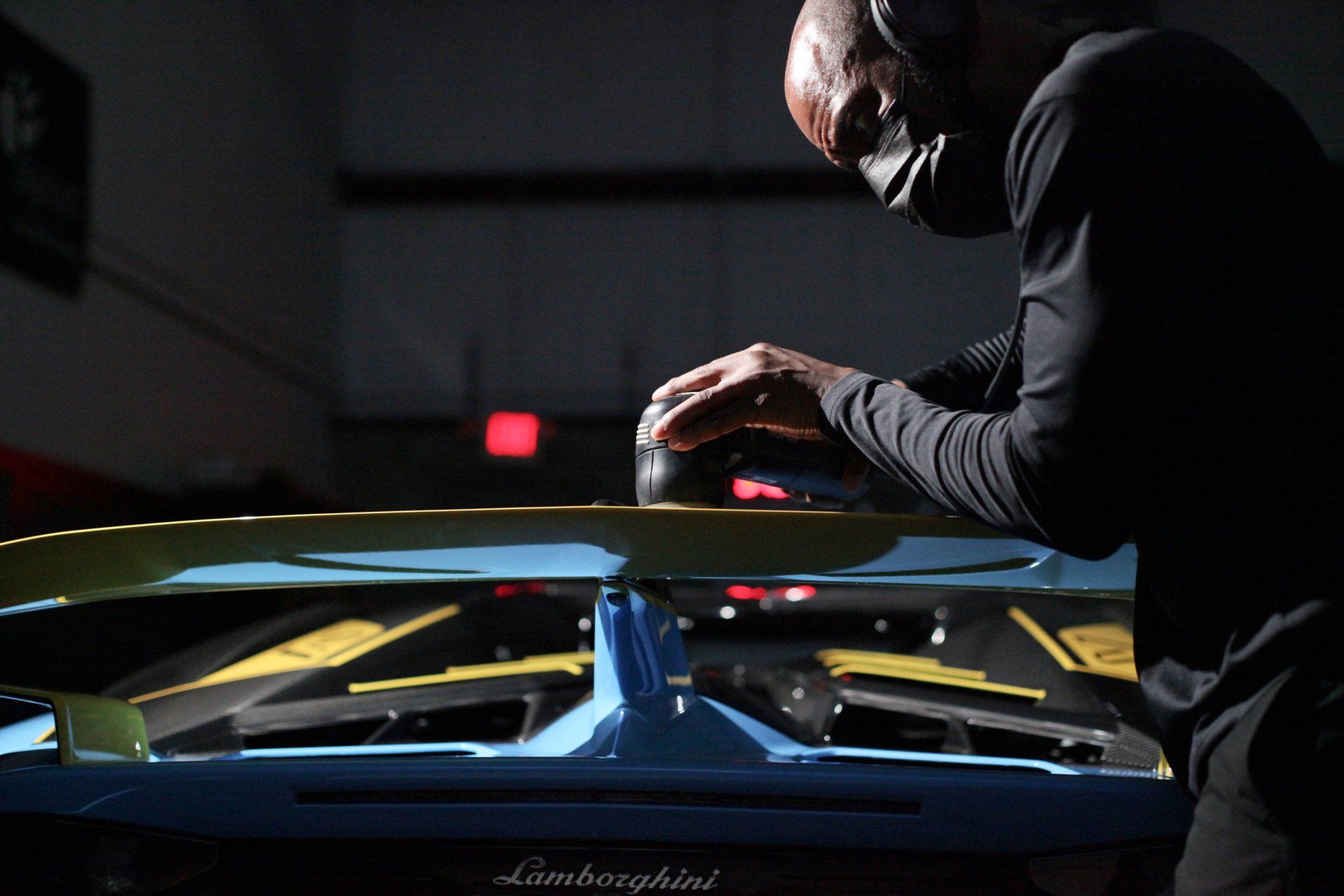 A man wearing headphones is working on a car in a dark room.