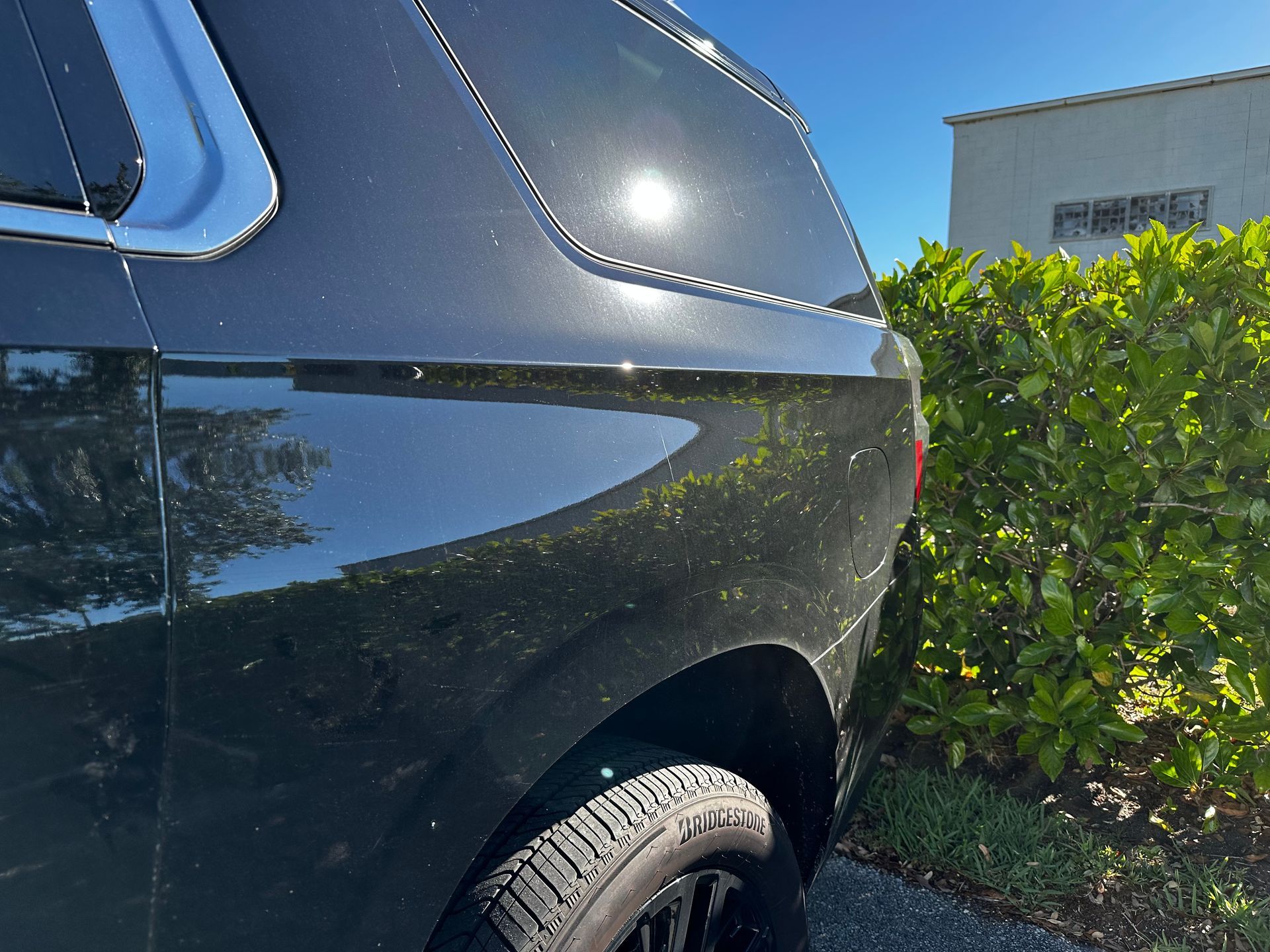 A black suv is parked in front of a hedge.