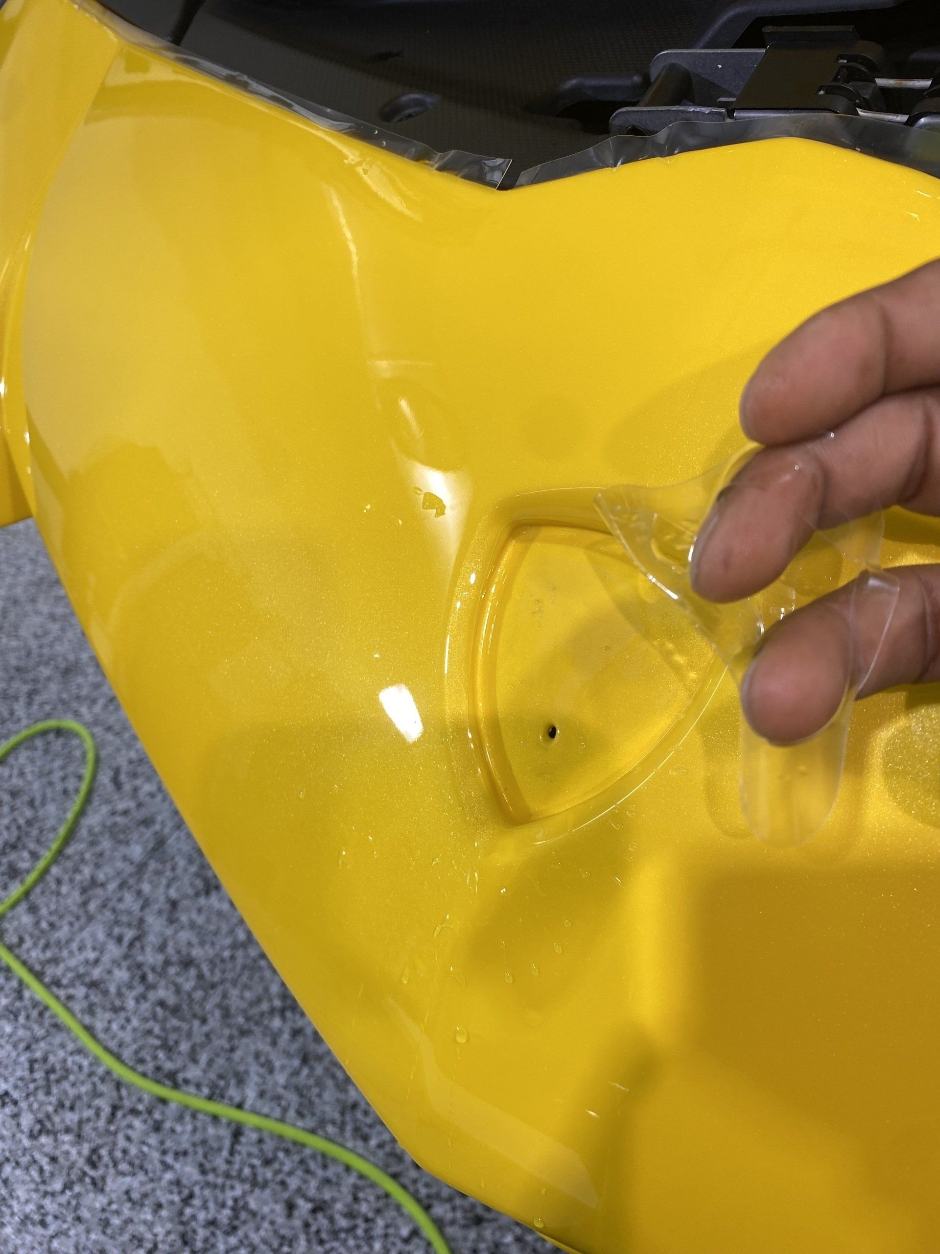 A person is holding a piece of plastic on a yellow car.