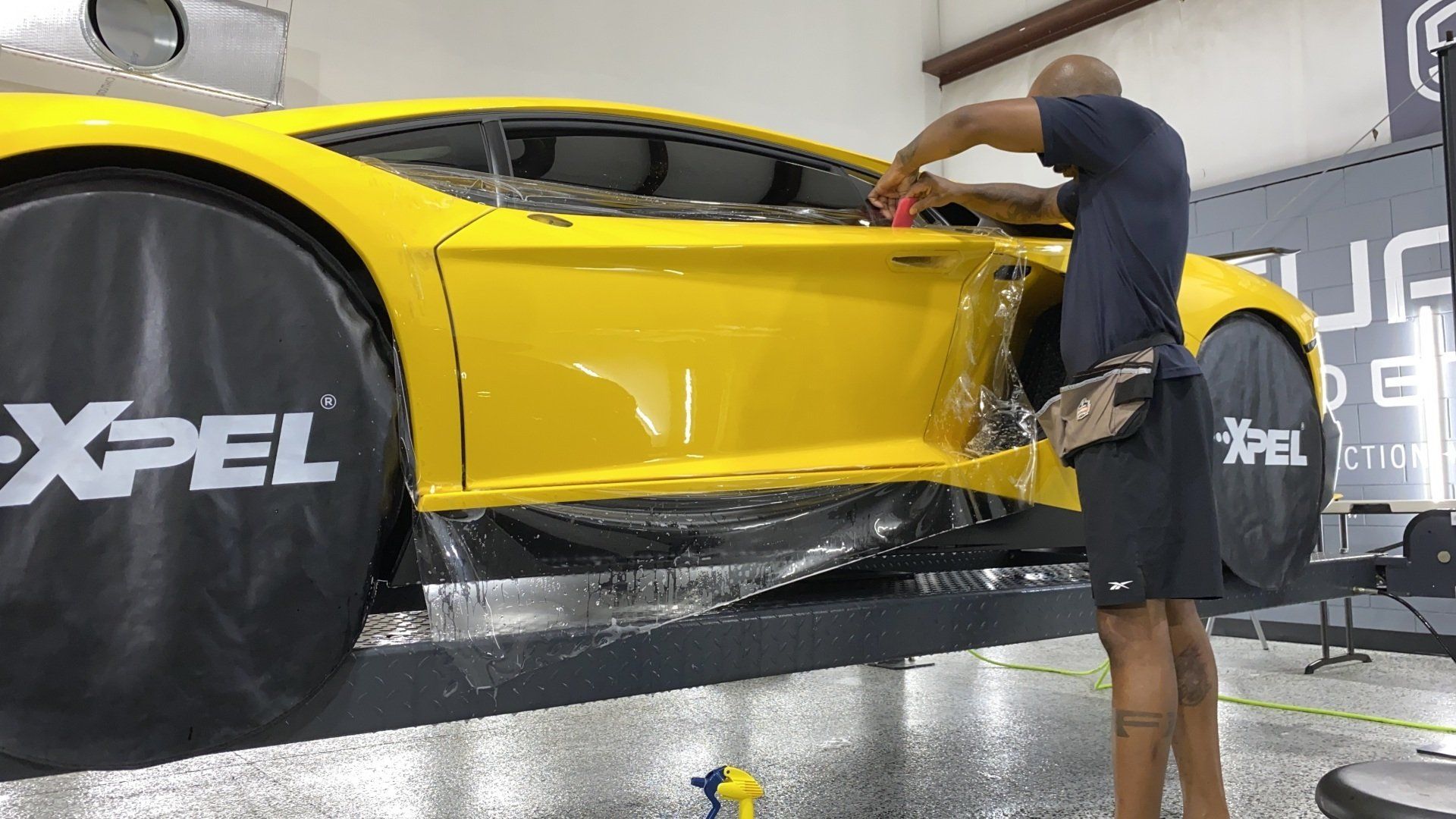 A man is wrapping a yellow sports car with xpel.