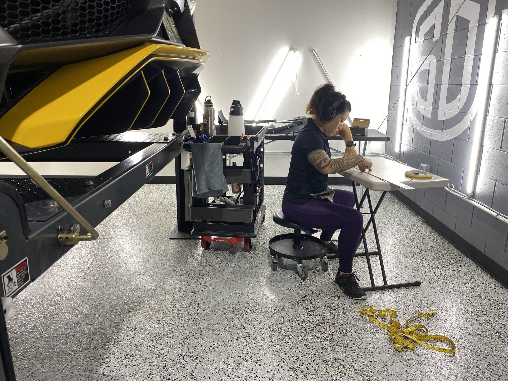 A woman is sitting at a table in a garage working on a boat trailer.