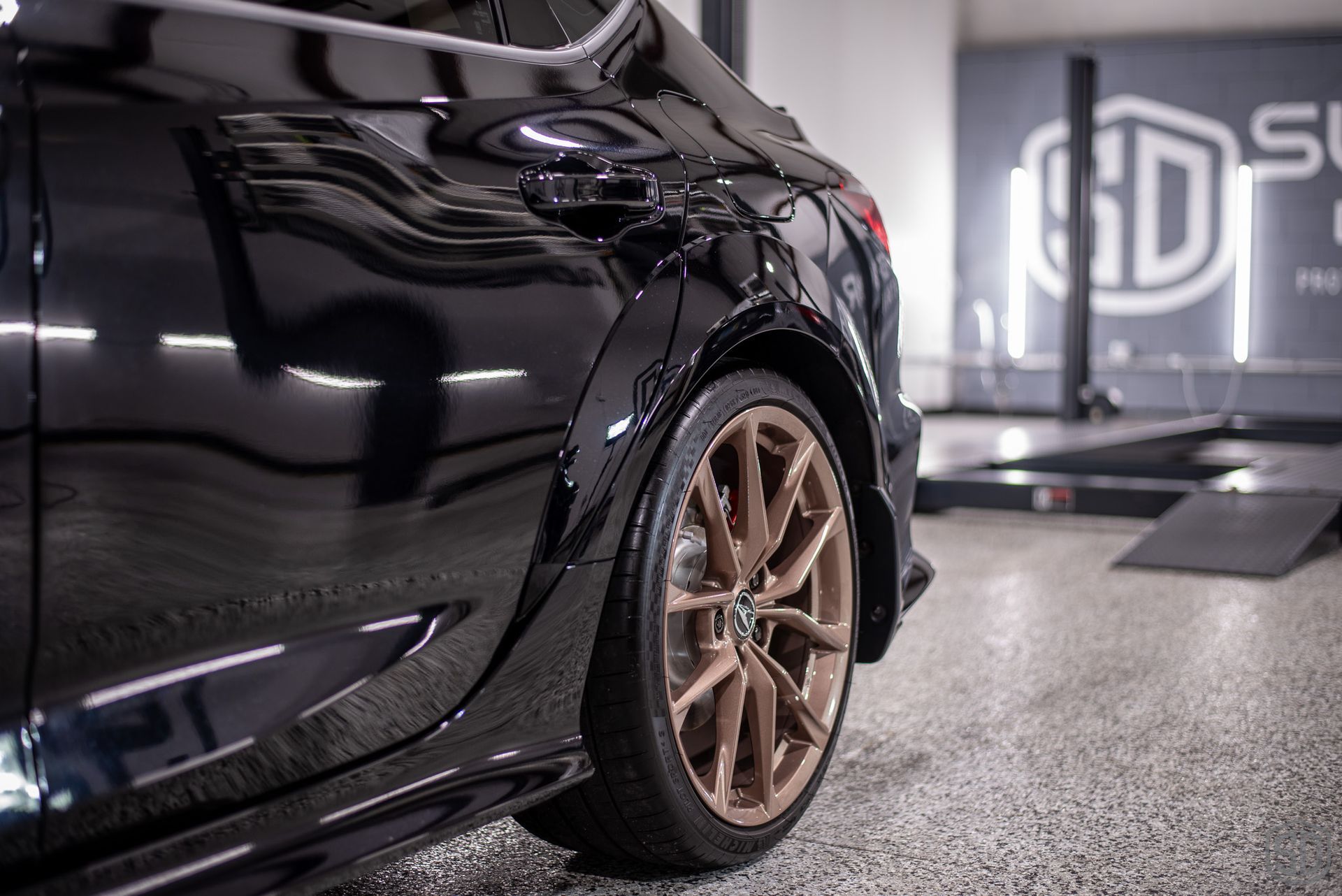 A blue car is parked on a black mat in a garage.