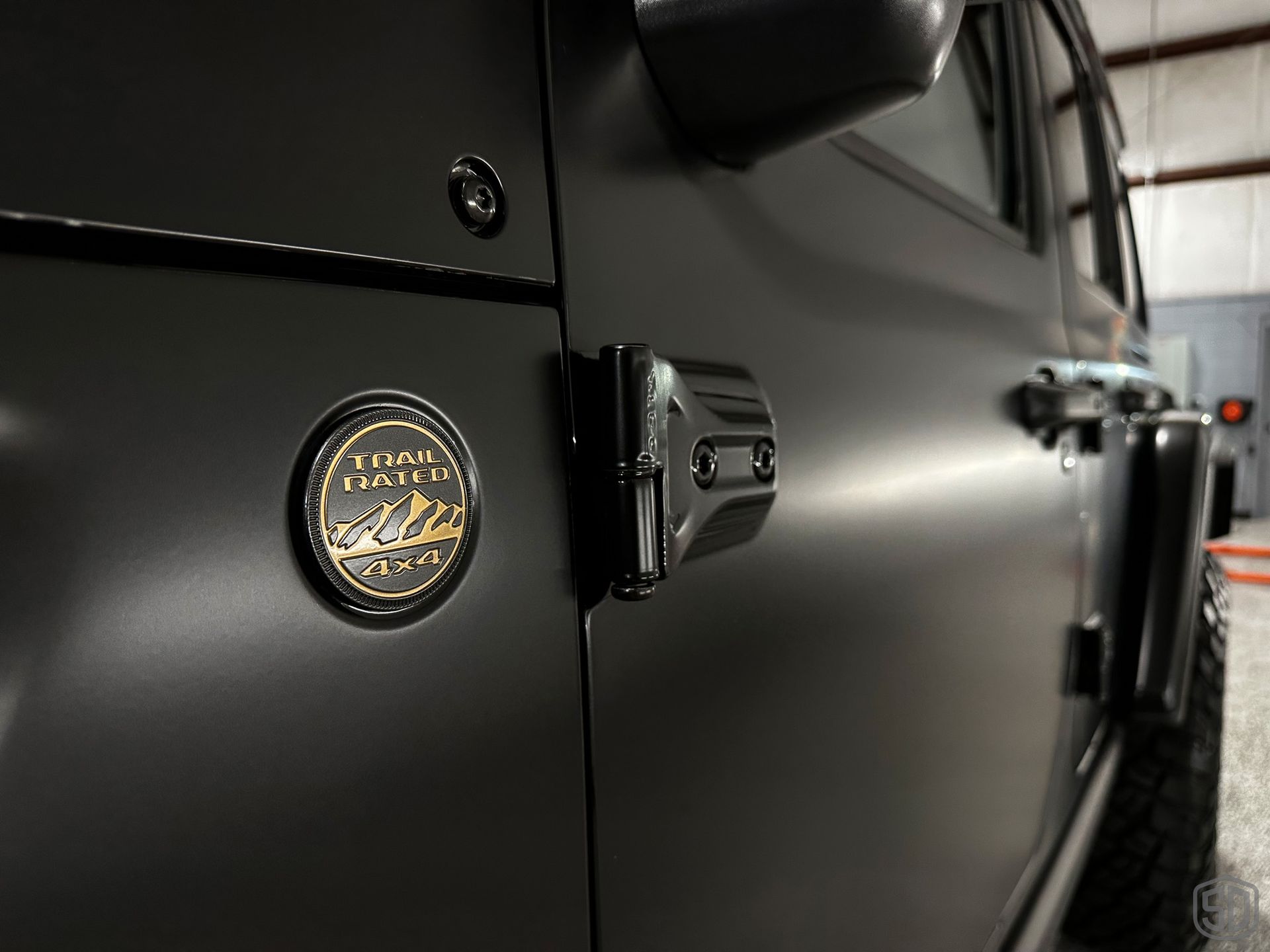 A black jeep with a gold emblem on the door is parked in a garage.