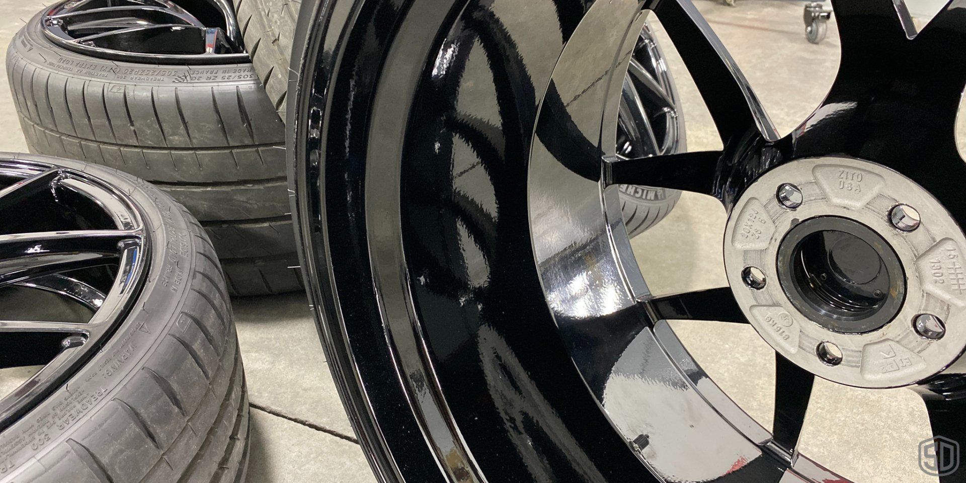 A close up of a black wheel with a tire in the background.