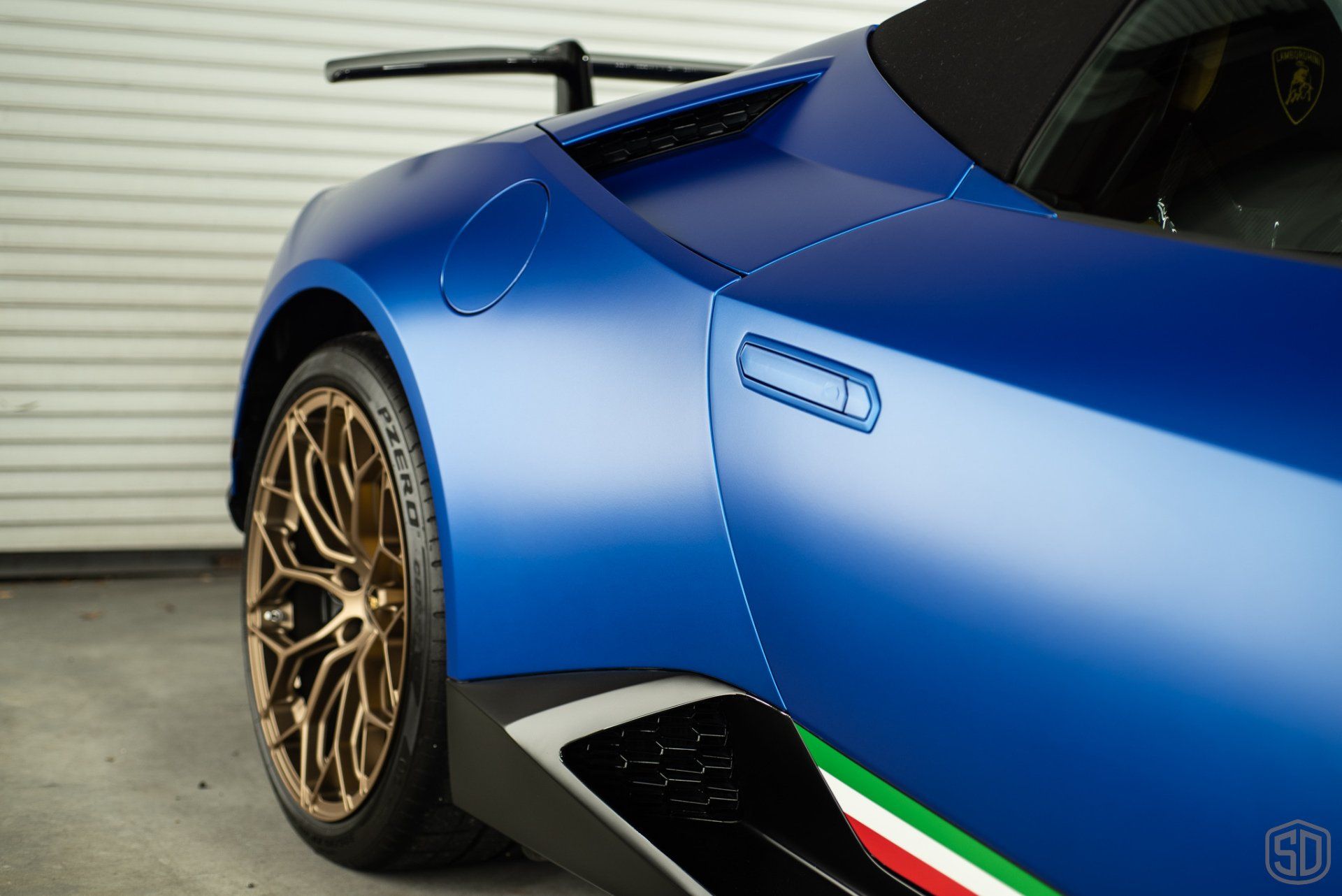 A blue sports car with gold wheels is parked in front of a garage door.