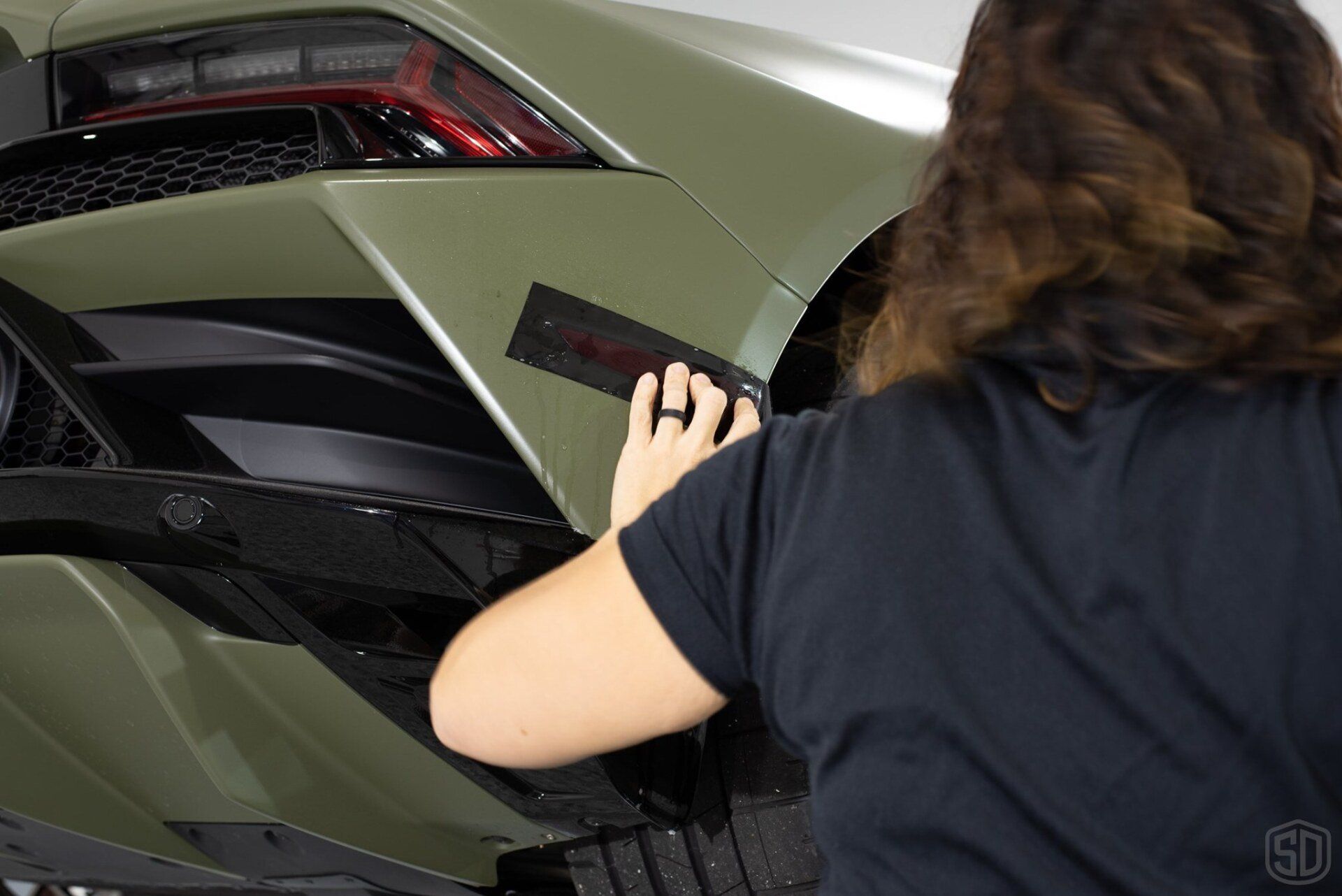 A woman is applying a sticker to the side of a car.