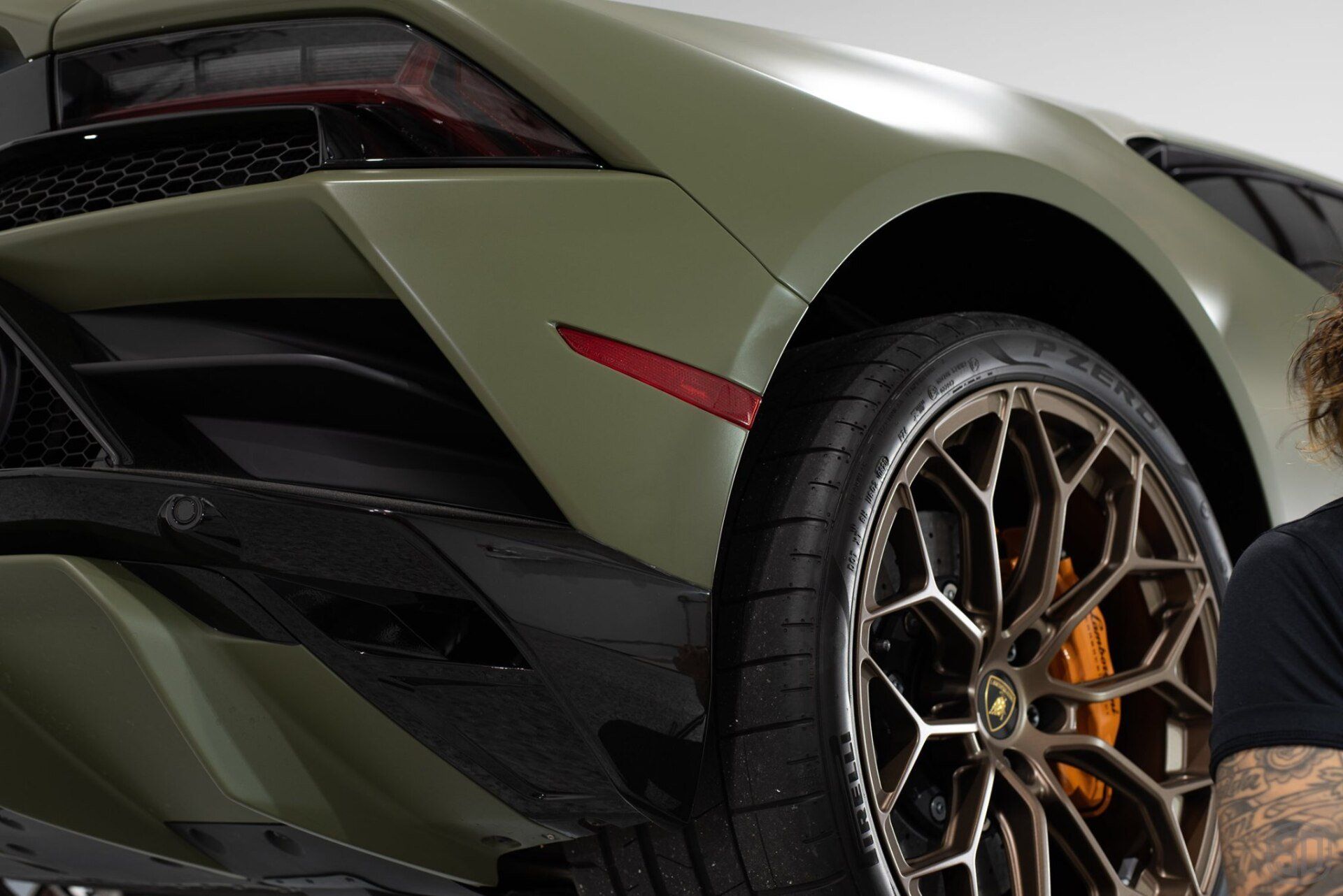 A man with a tattoo on his arm is standing next to a green sports car