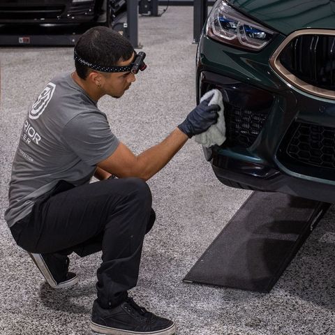 A man in a black shirt is smiling in front of a car.