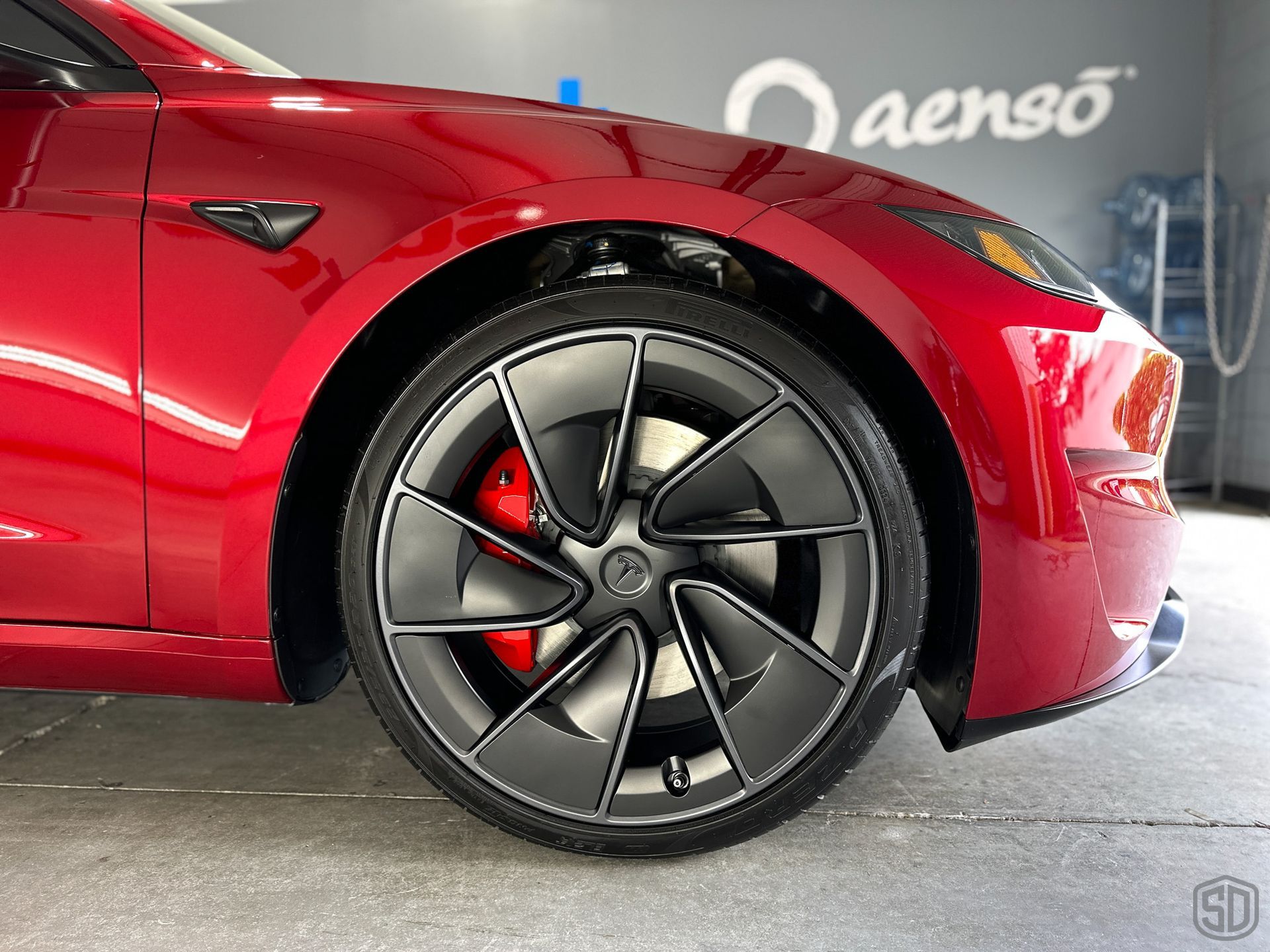 A red tesla model 3 is parked in a garage.