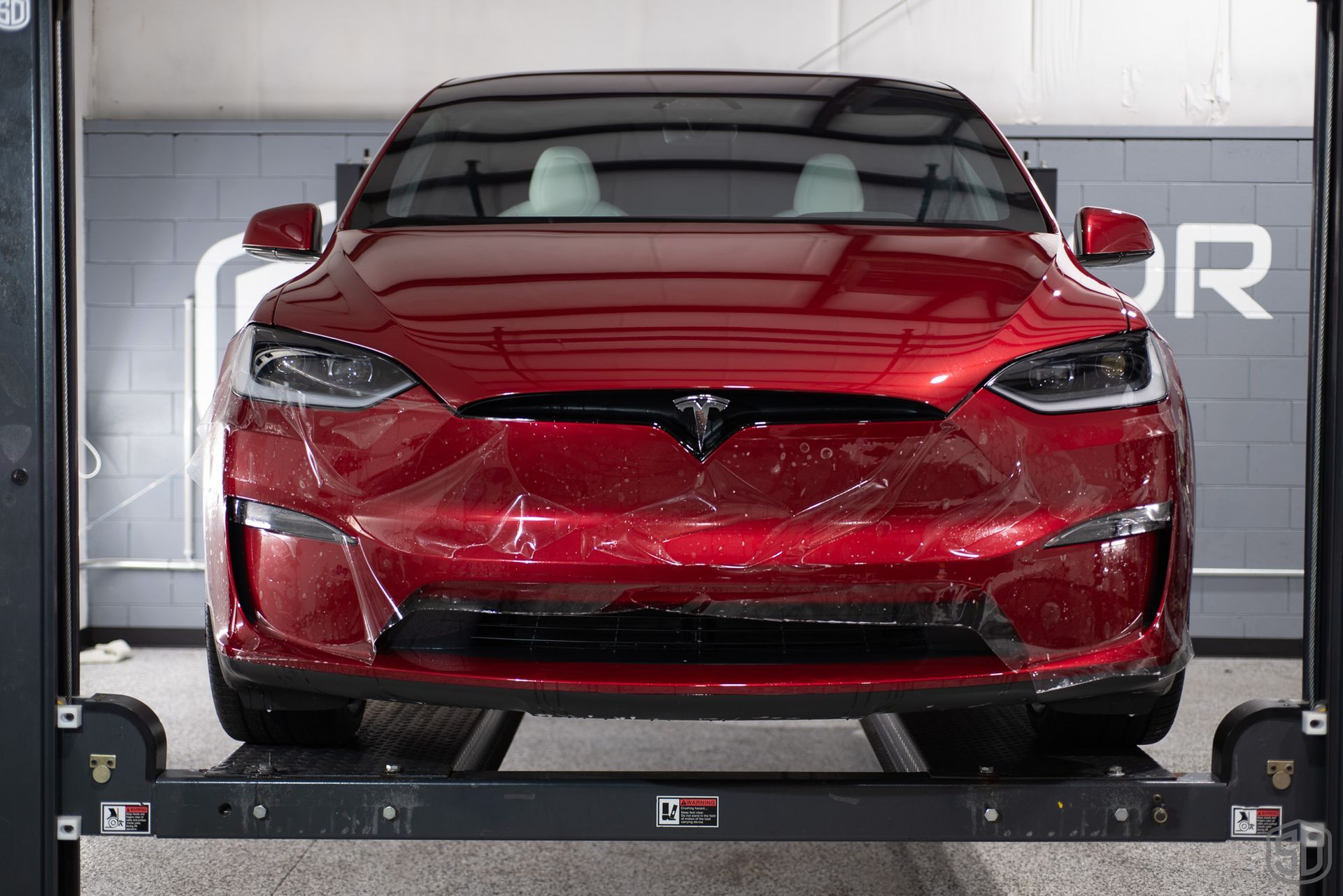 A red tesla's front bumper being wrapped with PPF
