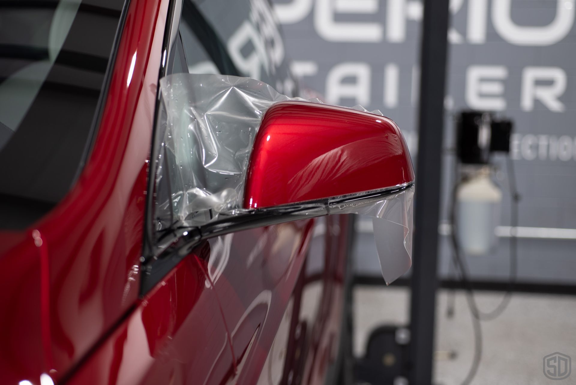 A red tesla's side mirror being wrapped in PPF