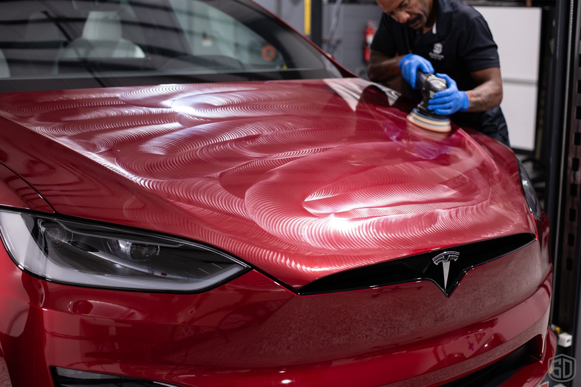 Karim polishing the hood of a red tesla model x.