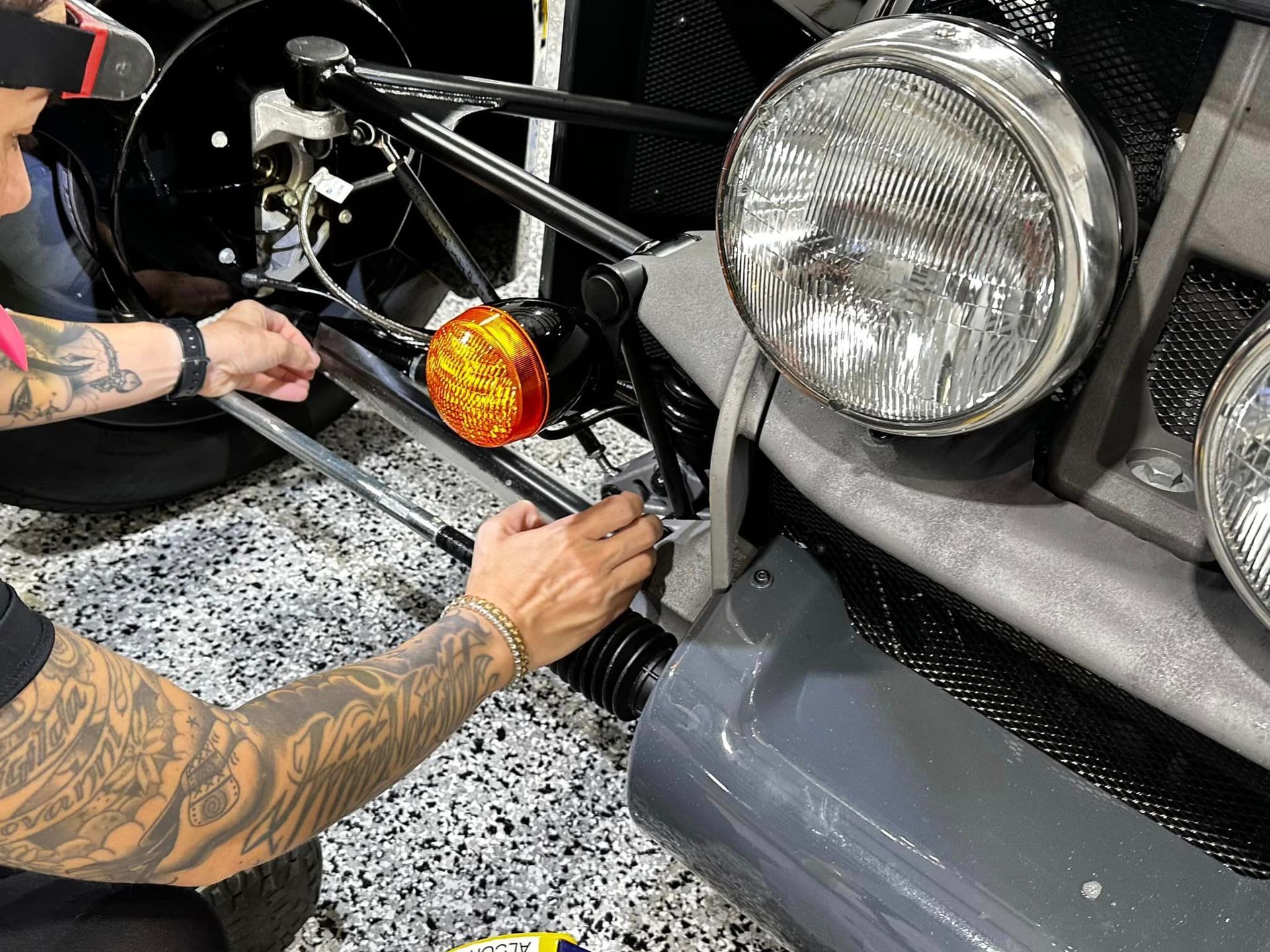 A man with tattoos is working on a car in a garage