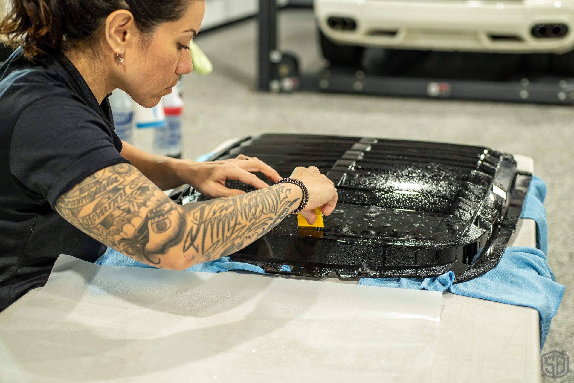 A woman with tattoos is working on a car in a garage.