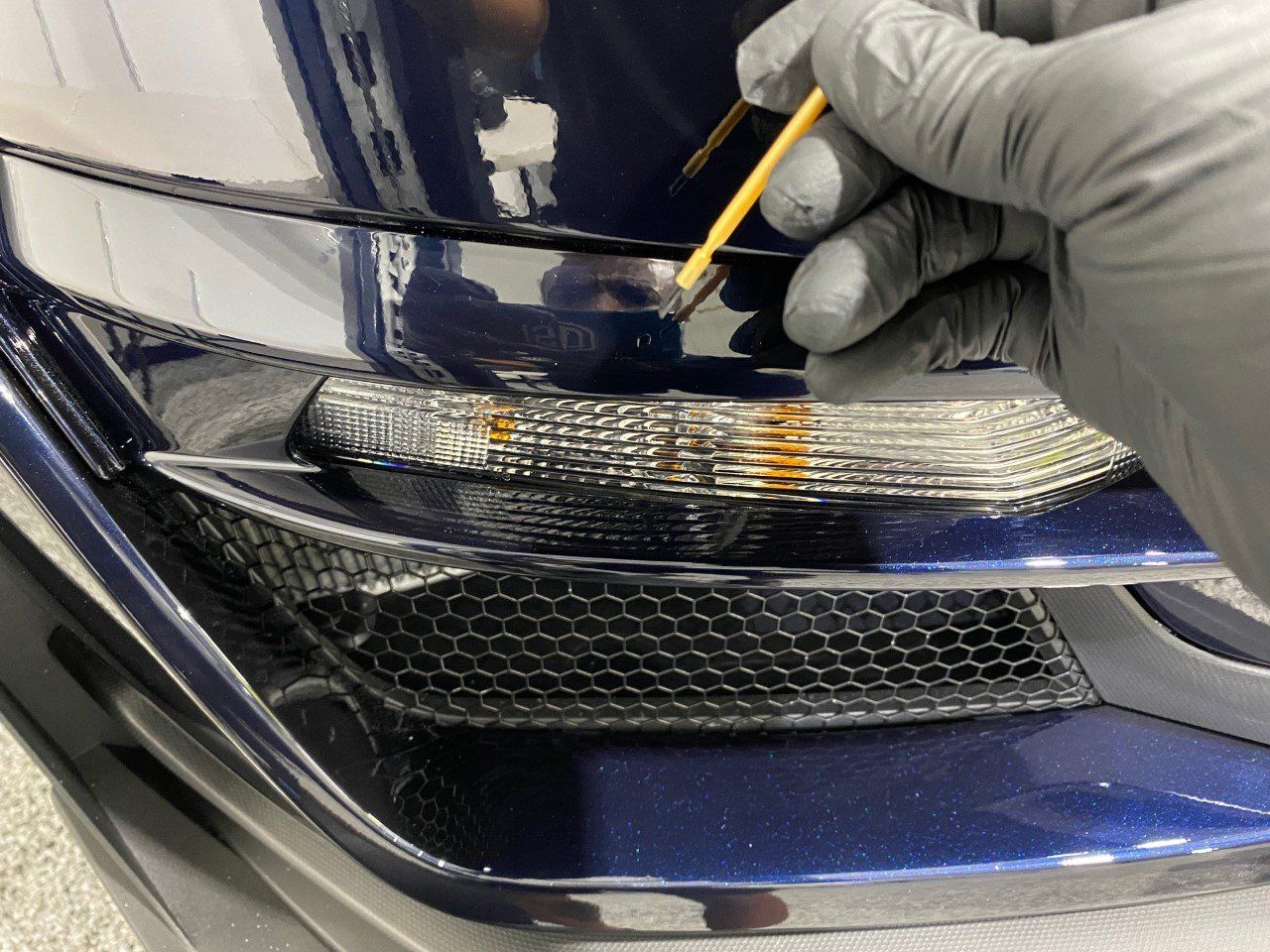 A person wearing gloves is painting the front of a car