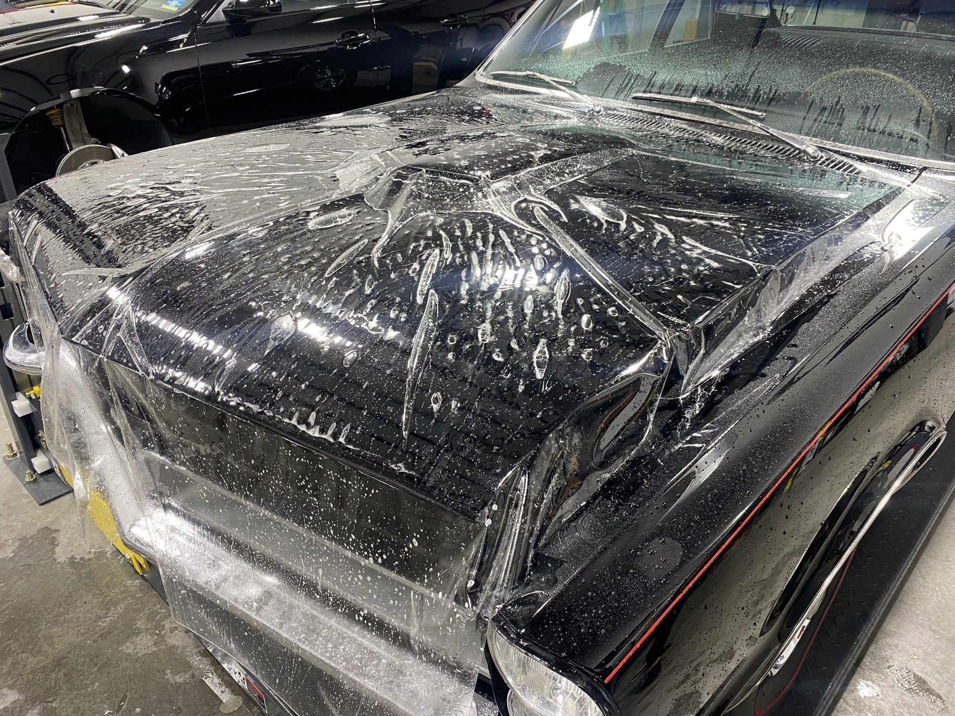 The hood of a black car is wrapped in plastic.