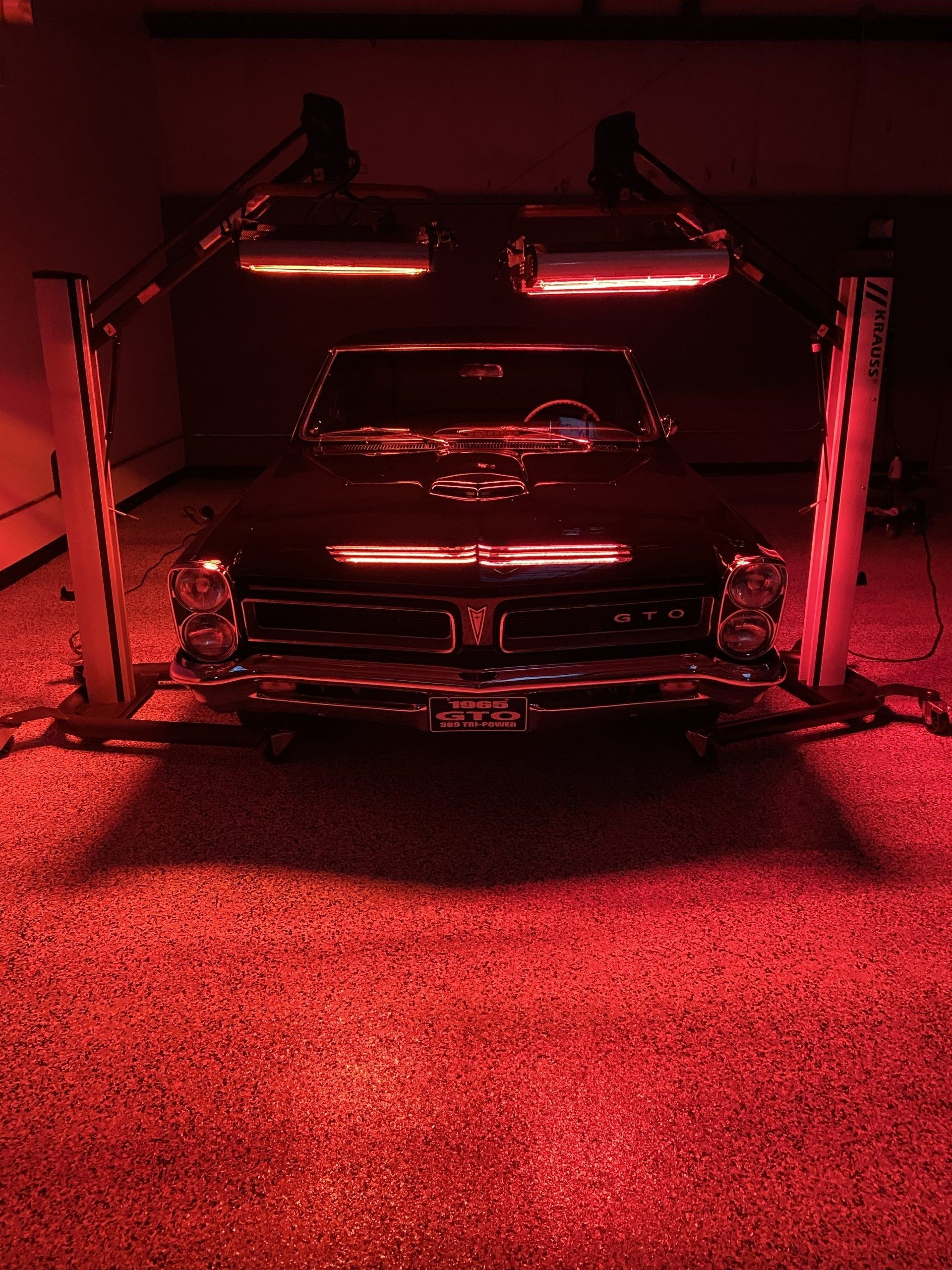 A black car is parked in a garage under red lights.