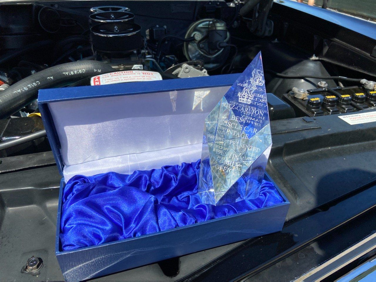 A blue box with a diamond in it sits under the hood of a car