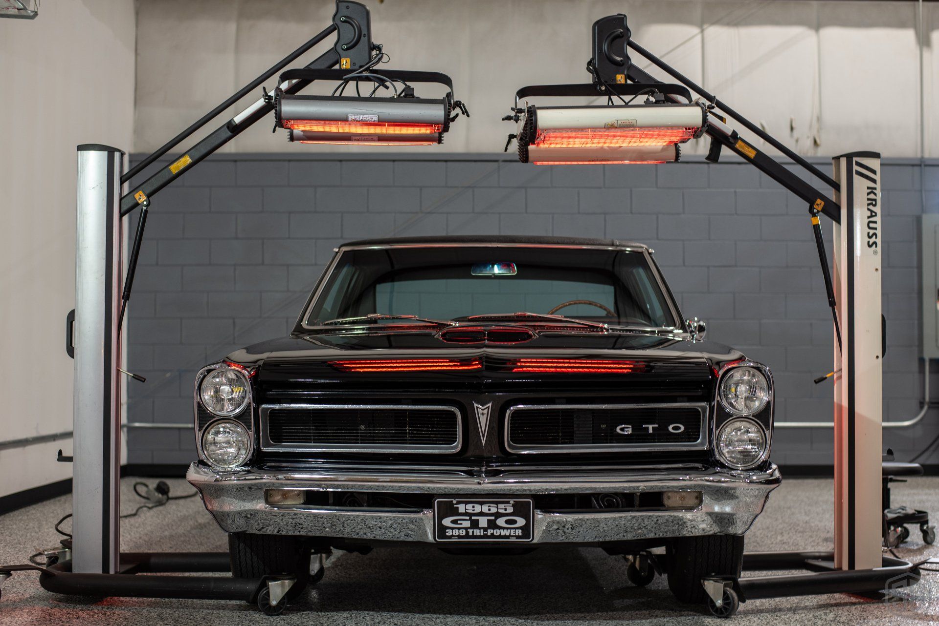 A black gto is parked in a garage under a heat lamp