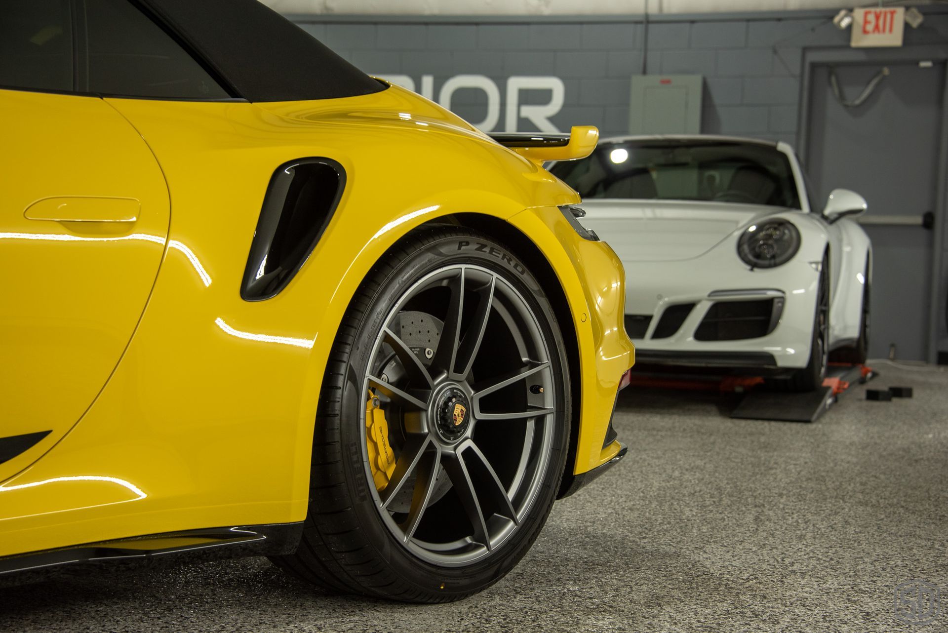 A yellow car is parked next to a white car in a garage.