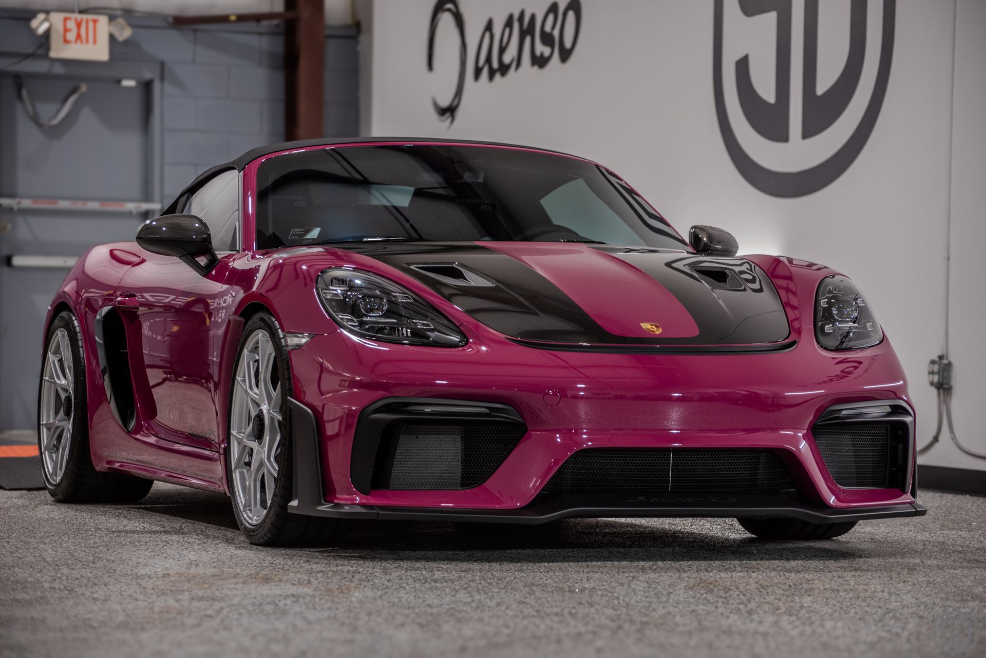 Pink and black Porsche sports car parked inside a garage, next to a logo.