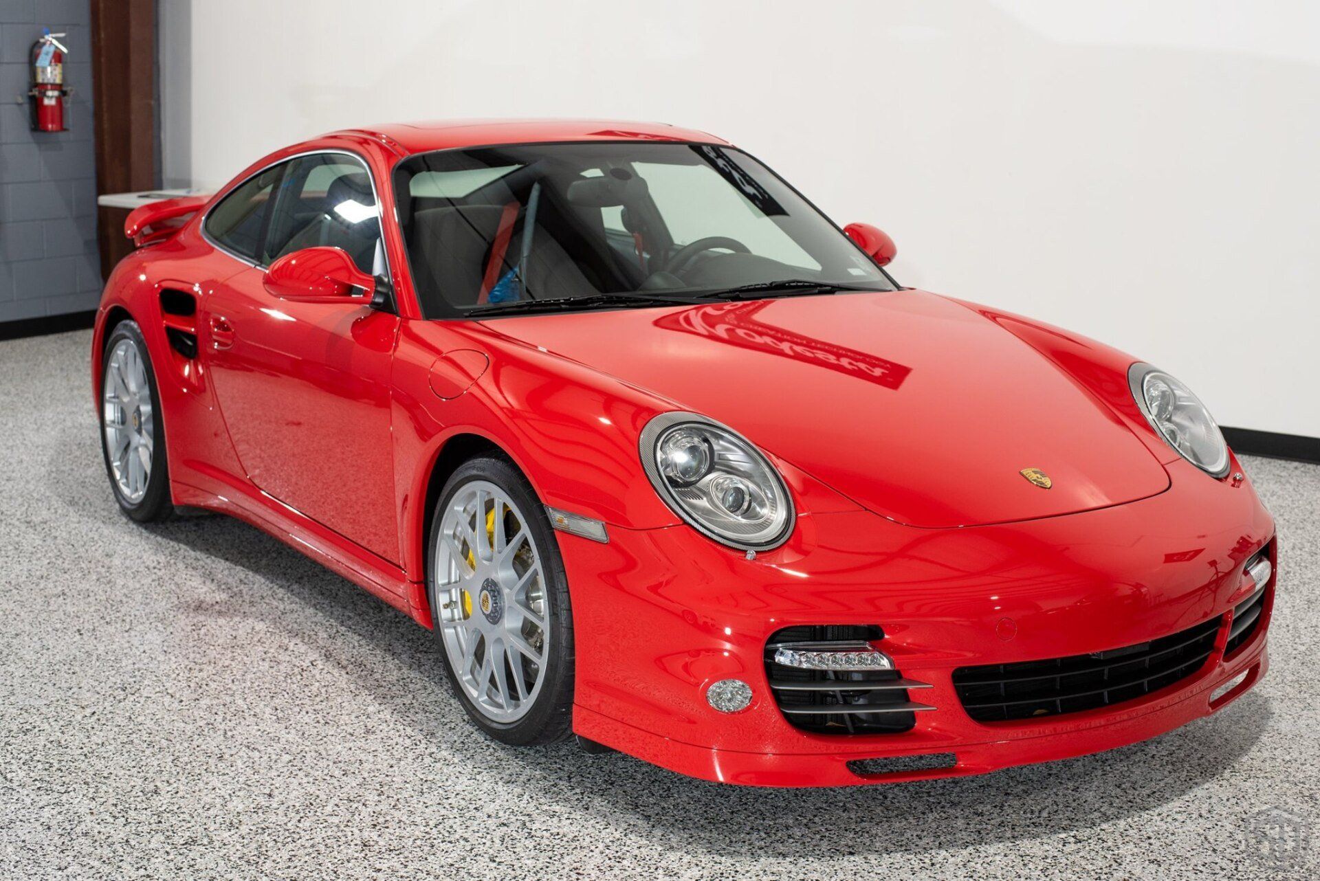 A red porsche 911 turbo is parked in a garage.