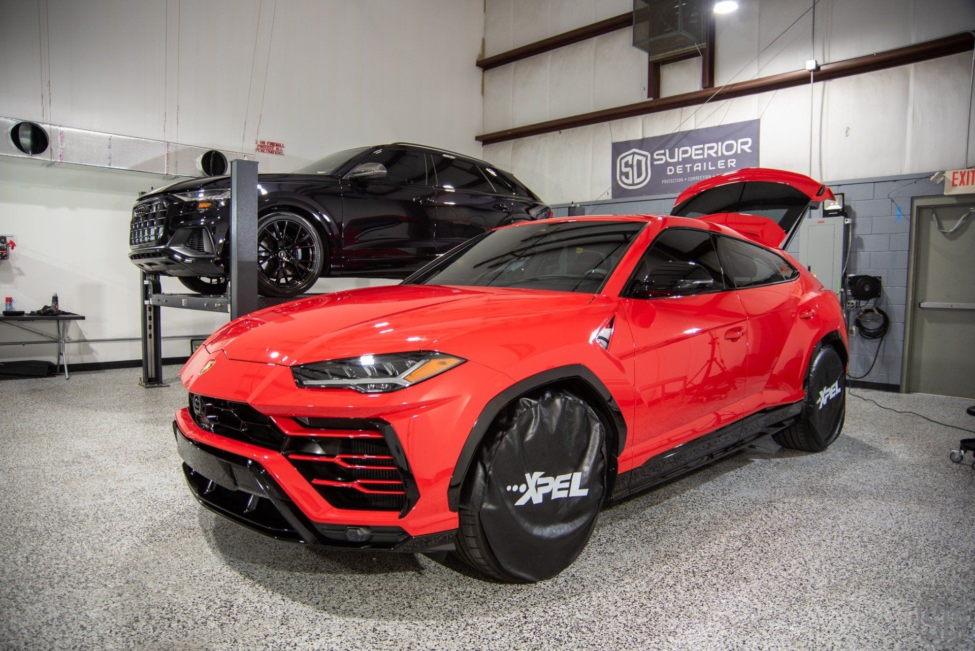 A red lamborghini urus is parked in a garage with its hood up.