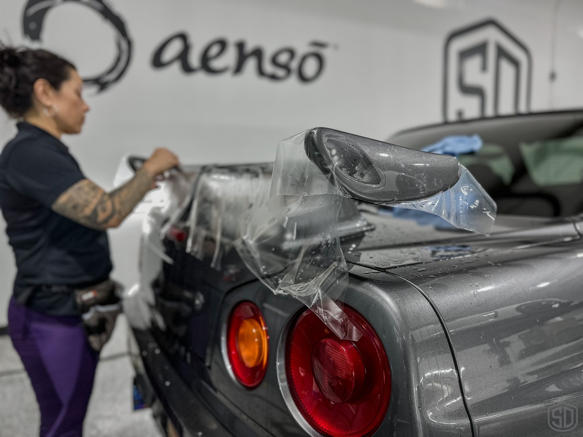 A woman is wrapping a car with plastic wrap.