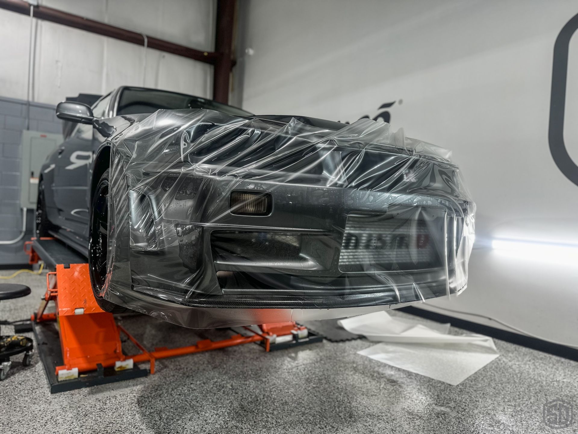 A car is wrapped in plastic and sitting on a lift.