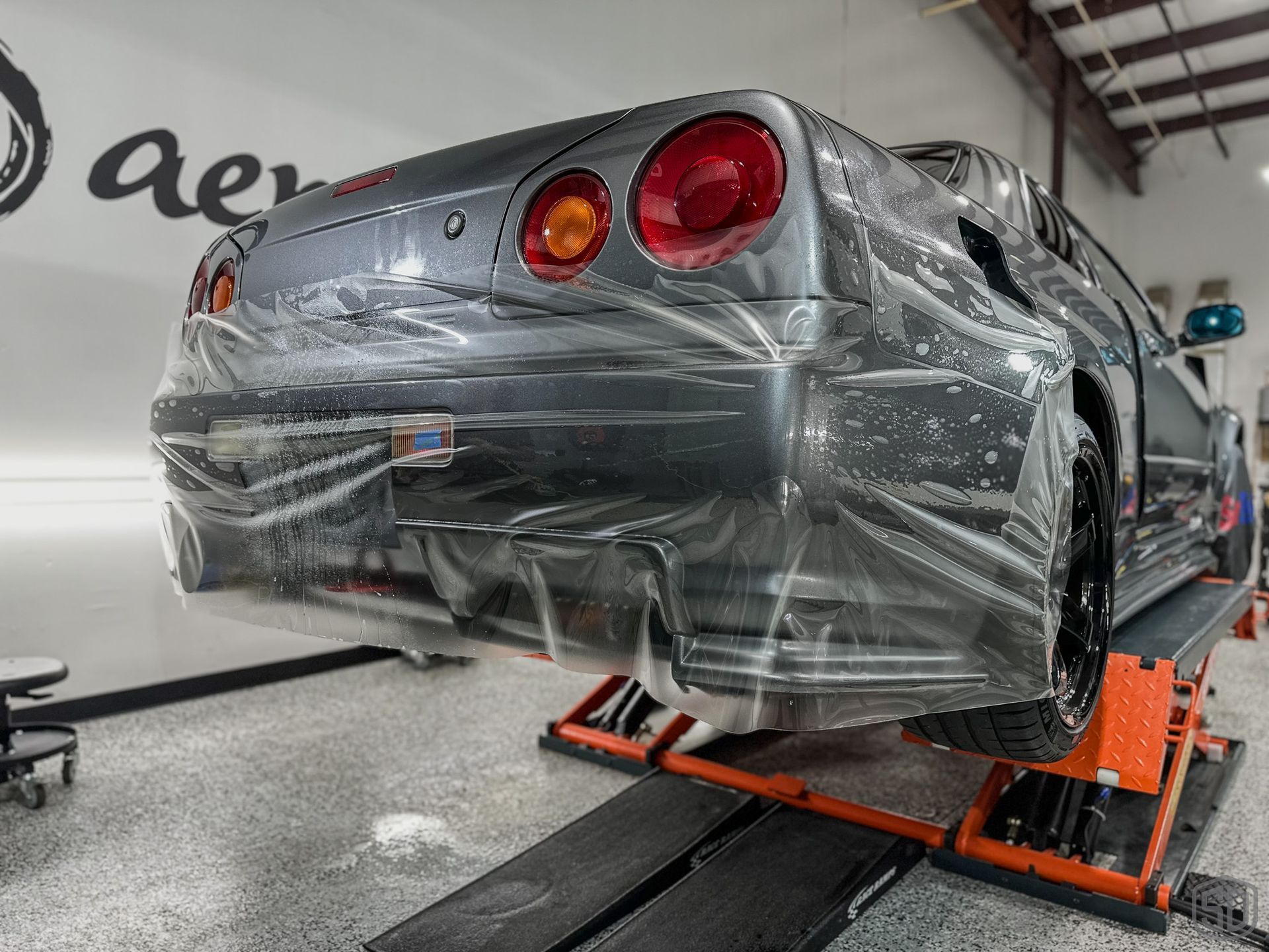 A car is wrapped in plastic and sitting on a lift.