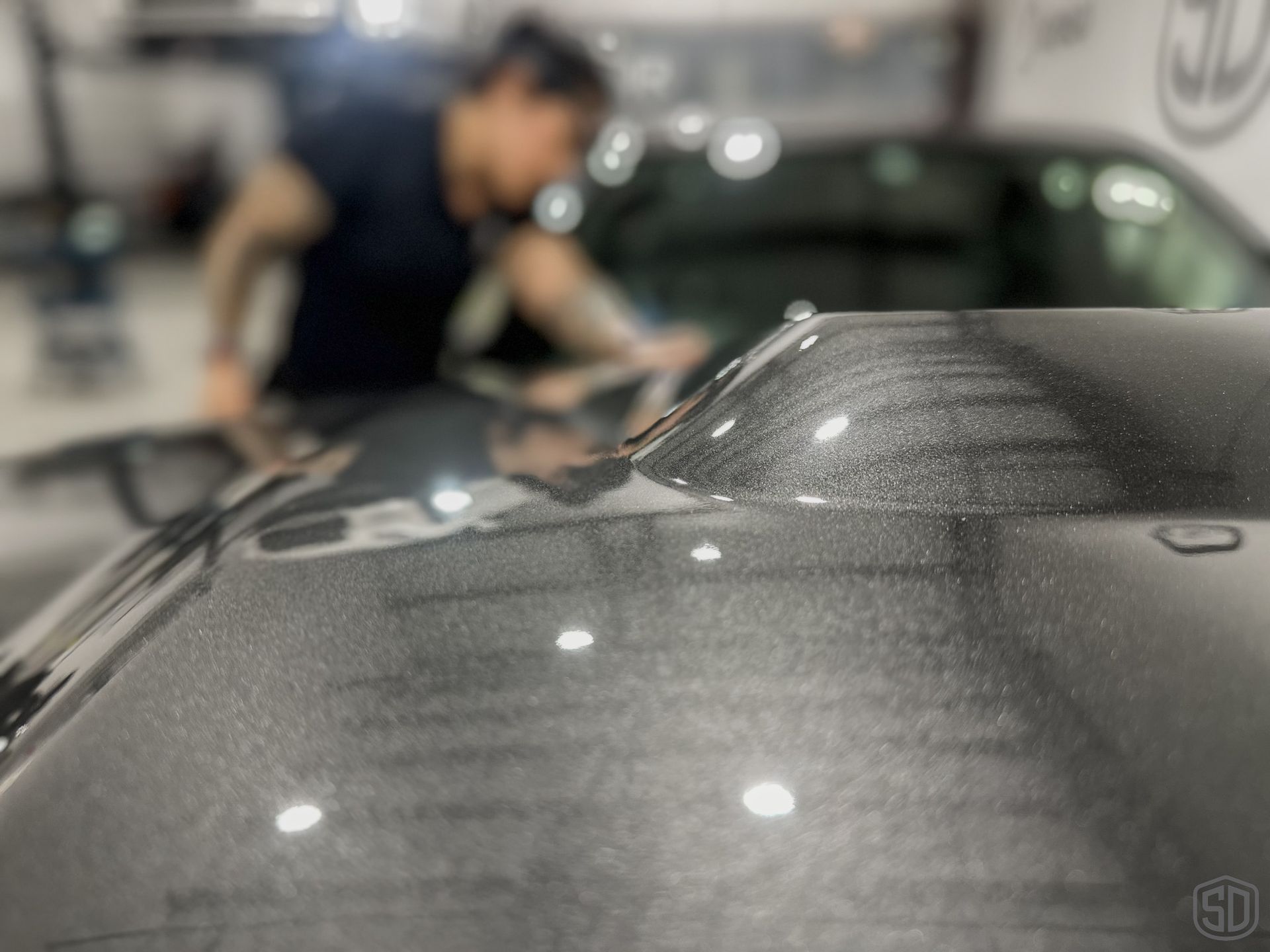 A man is cleaning the windshield of a car in a garage.