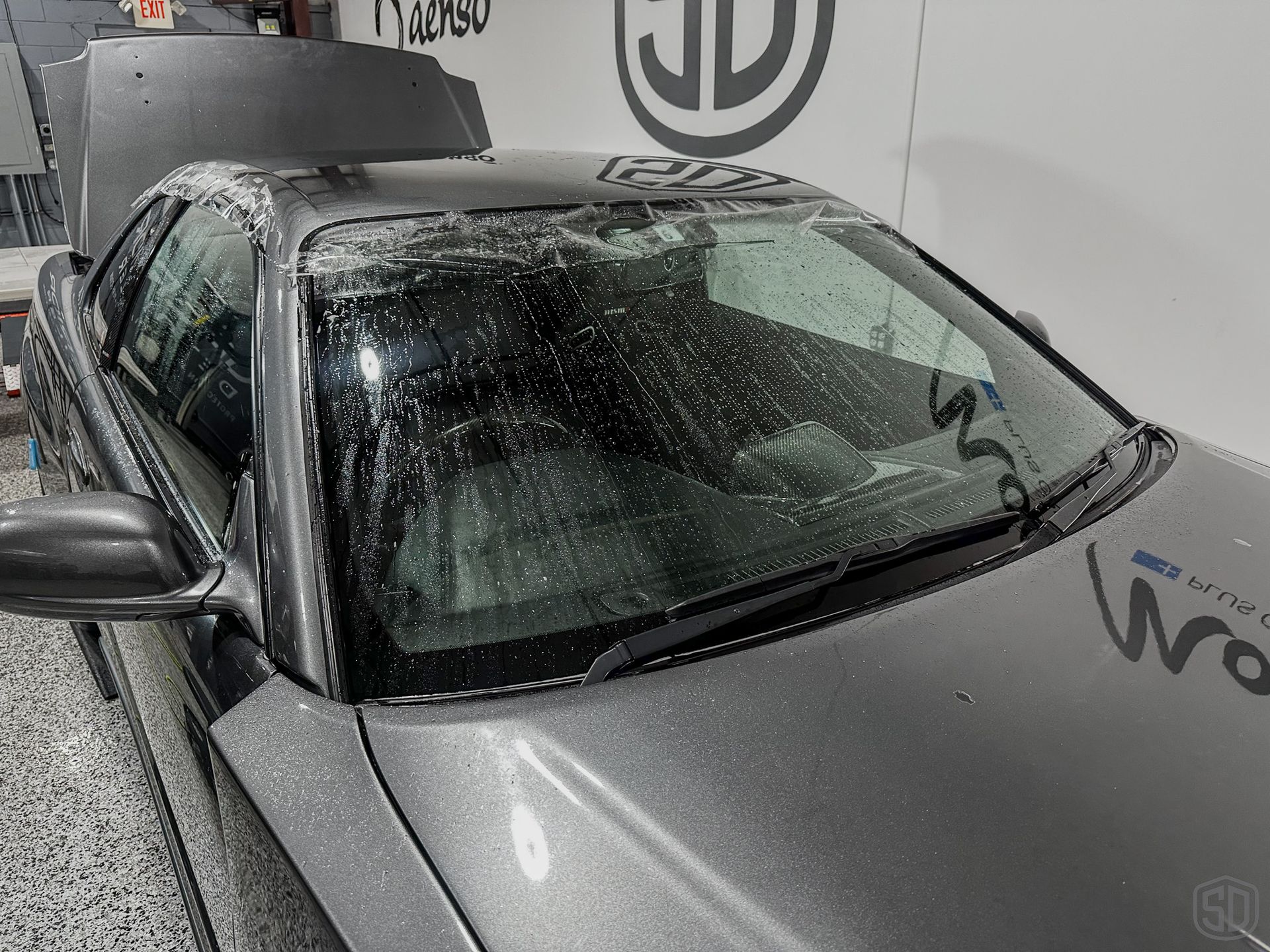 A gray sports car with a broken windshield is parked in a garage.